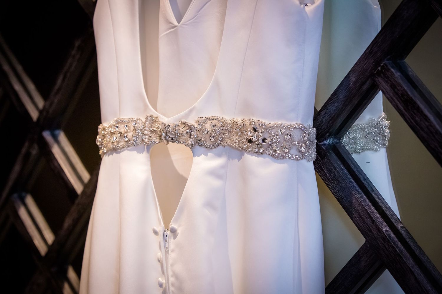 Close-up details of a white wedding dress showing intricate beaded belt and button details.