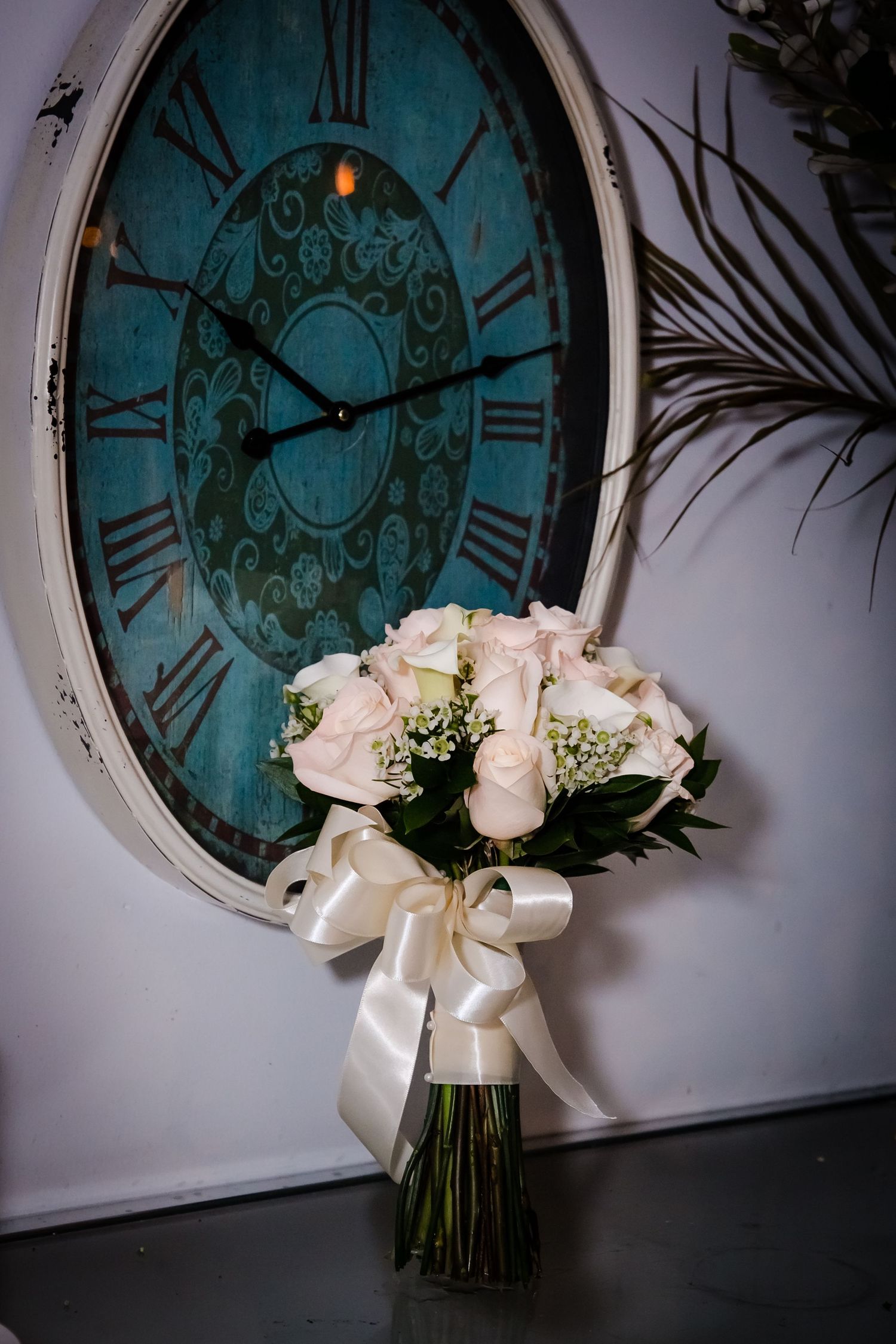 White rose wedding bouquet arranged against vintage turquoise clock backdrop.