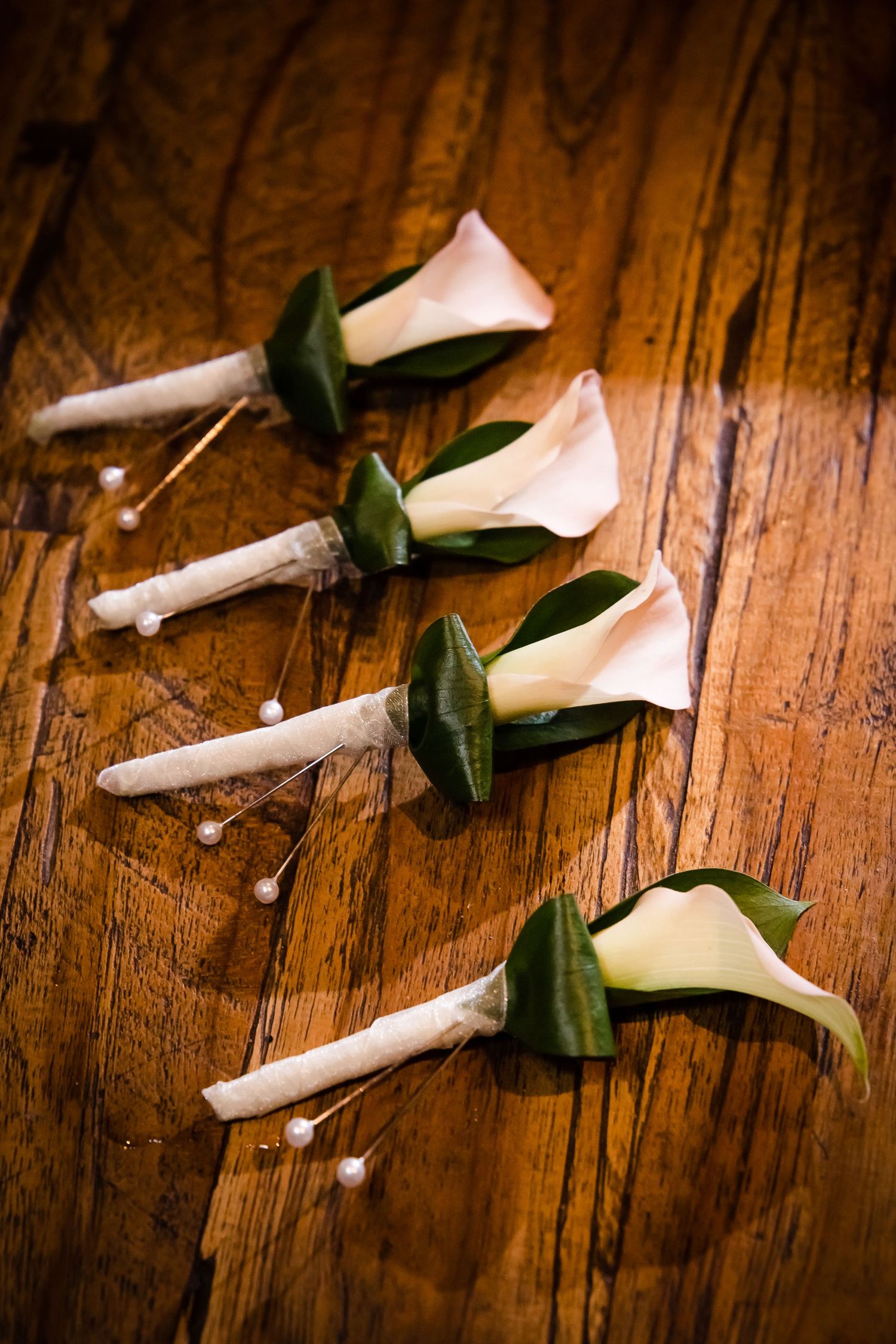 White calla lily flowers with green stems arranged on a rustic wooden surface.