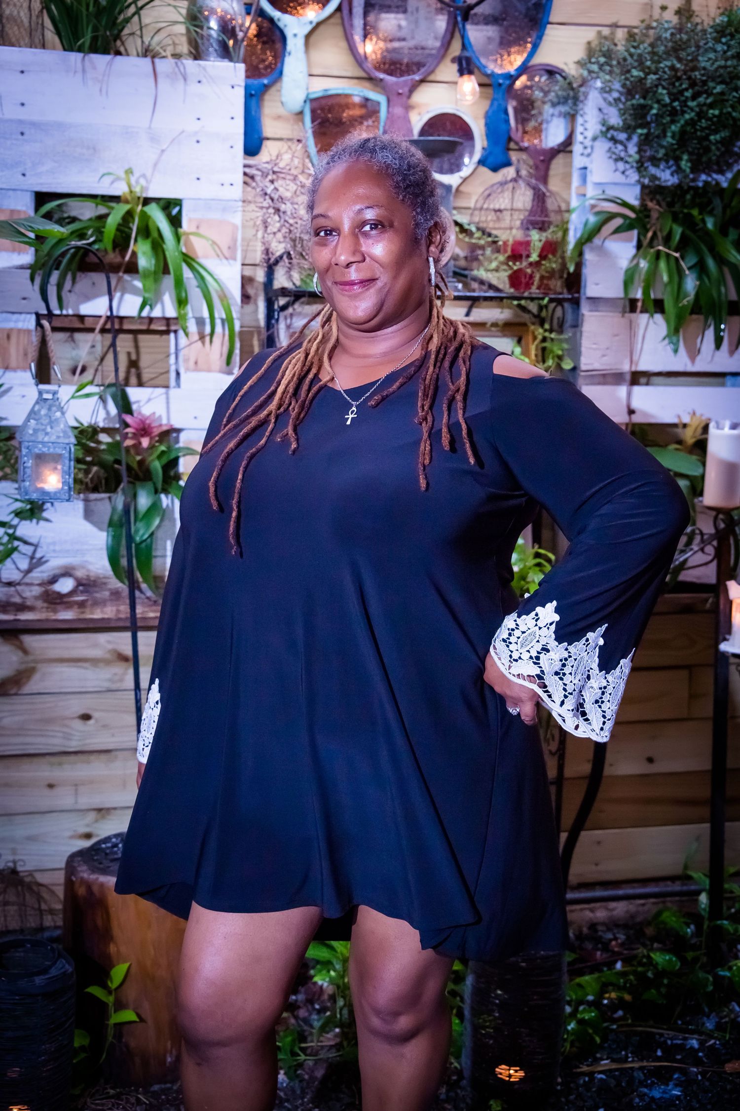 Someone wearing a black dress poses playfully in an outdoor garden setting.