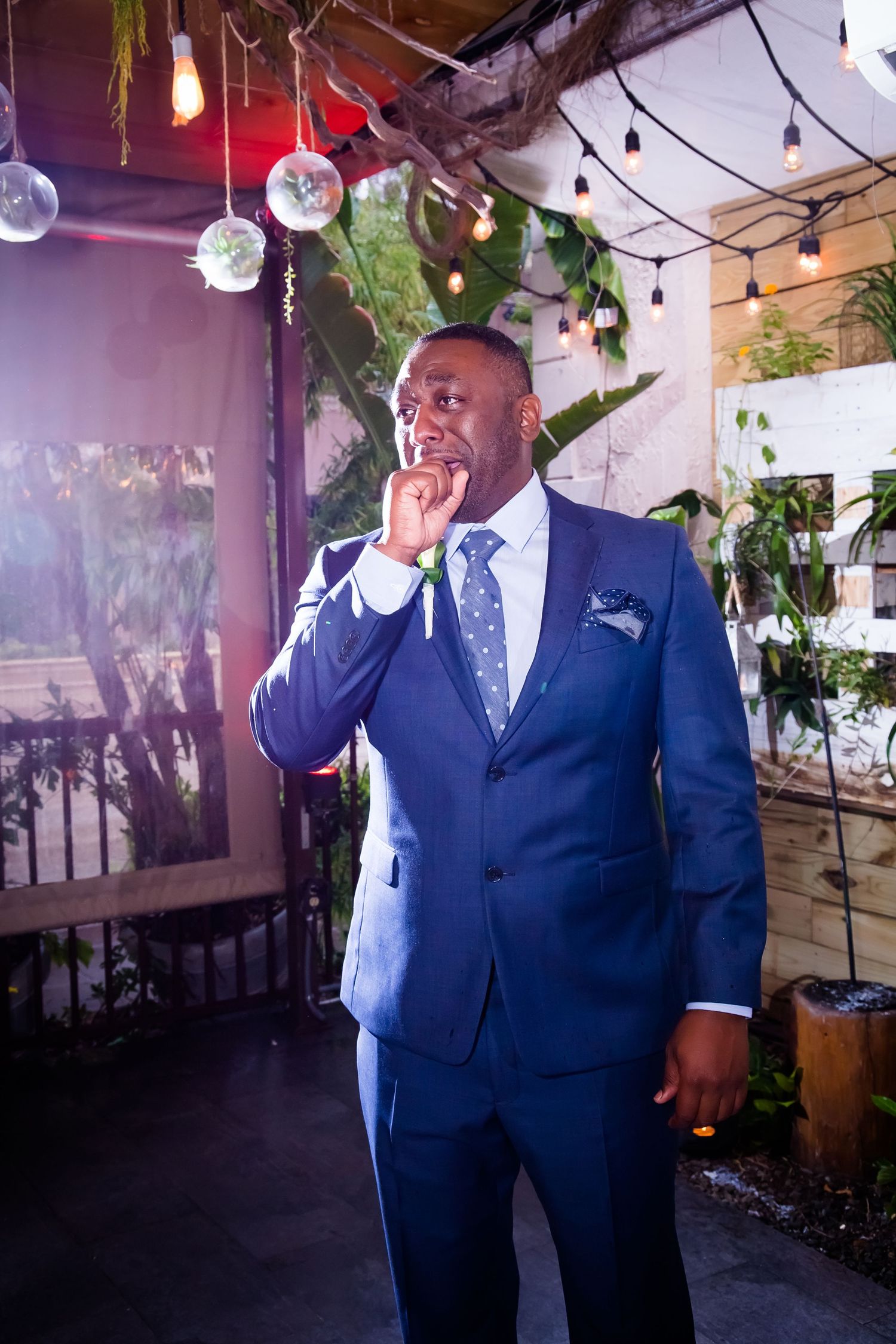 A guest in a navy blue suit shows emotion during a wedding celebration.