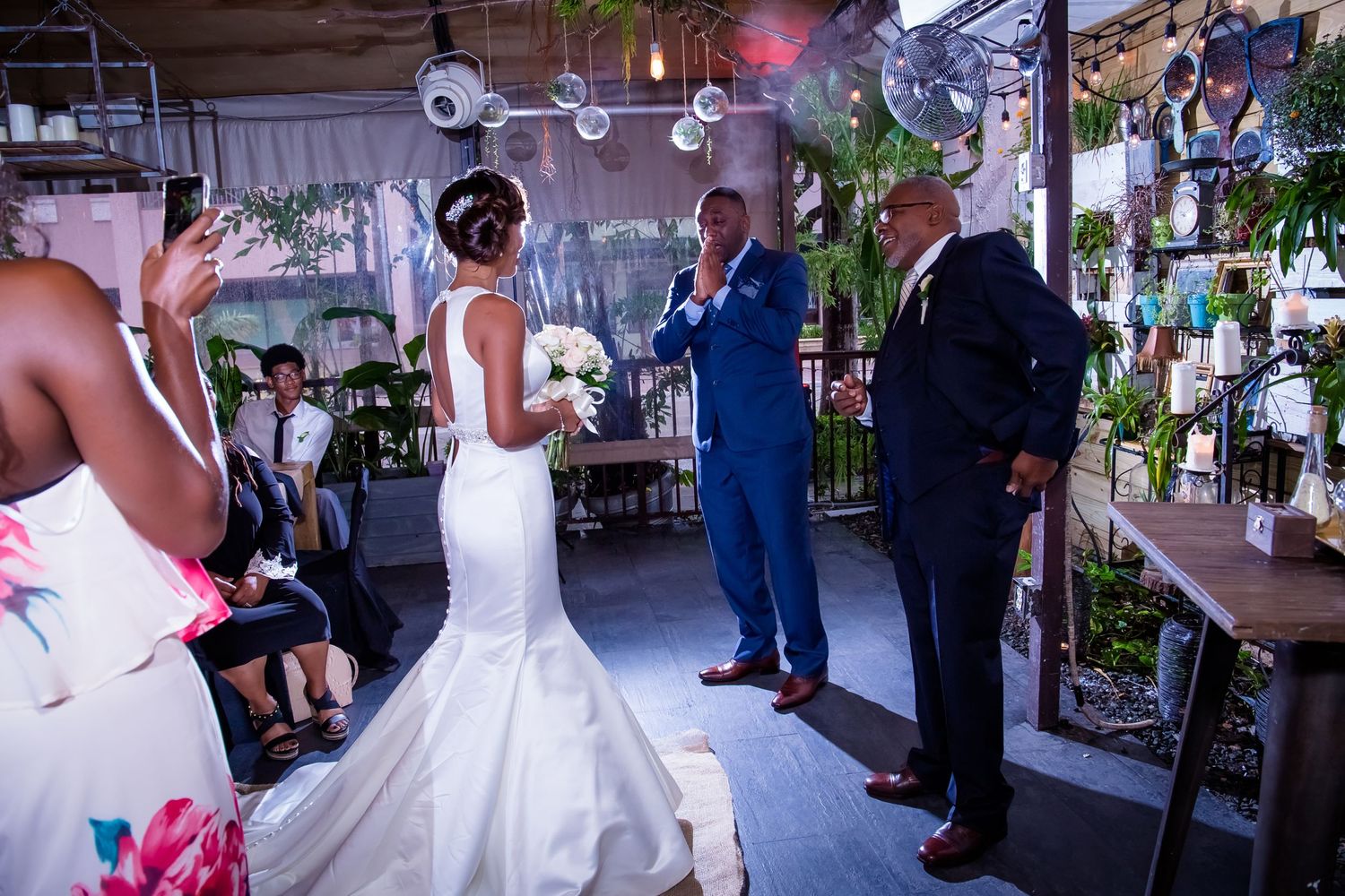 Wedding ceremony in a decorated indoor venue with hanging lights and greenery.