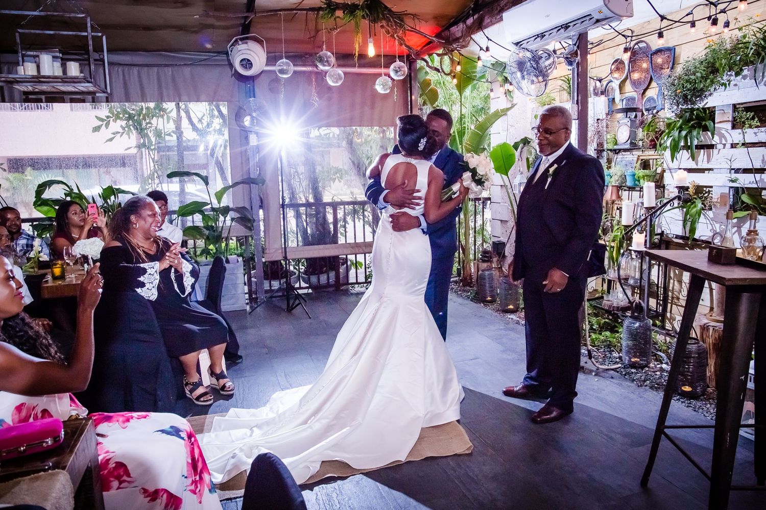 Couple exchanges vows in an industrial-style venue decorated with plants and string lights.