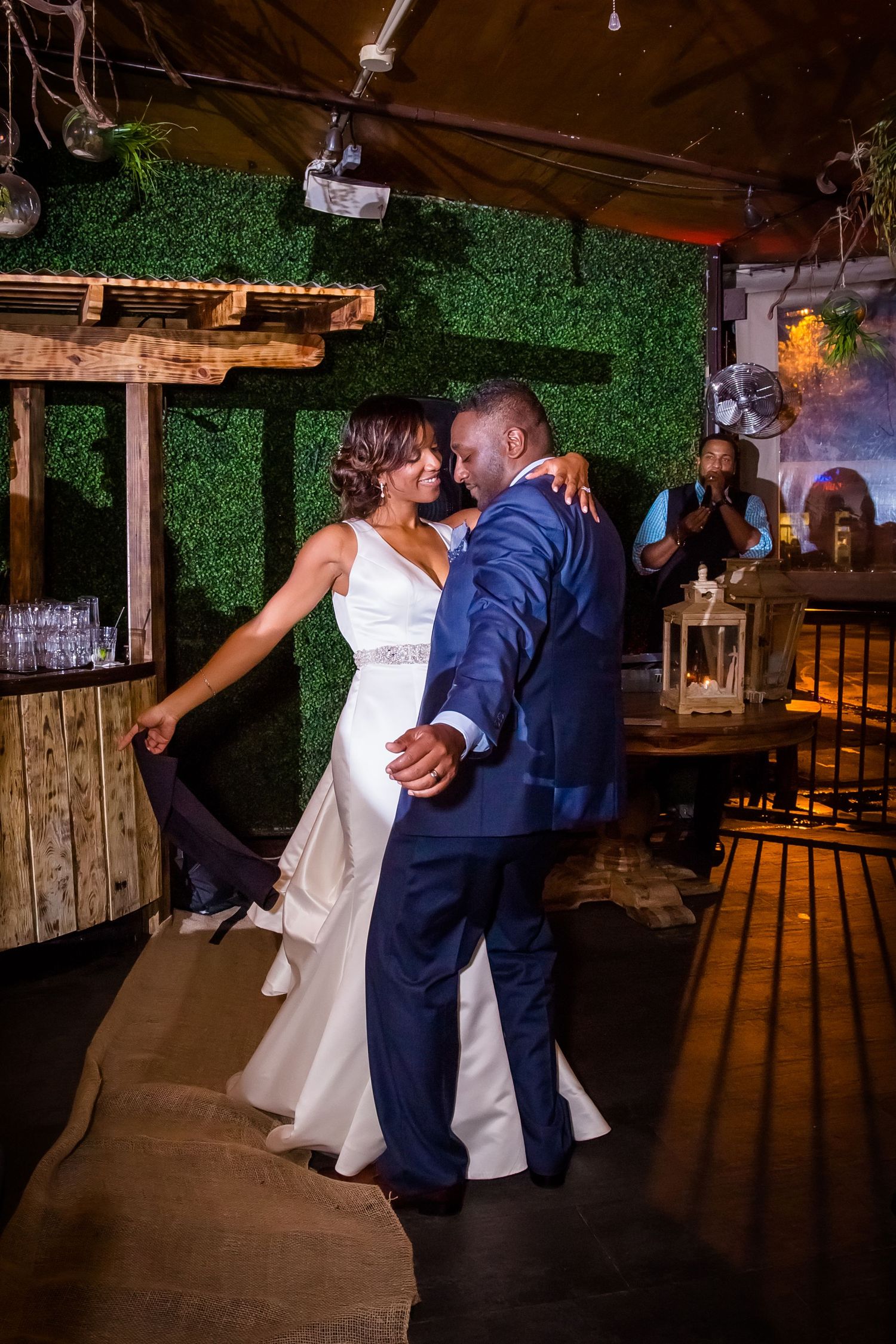 Bride and groom dancing together in a rustic venue with green wall decorations.