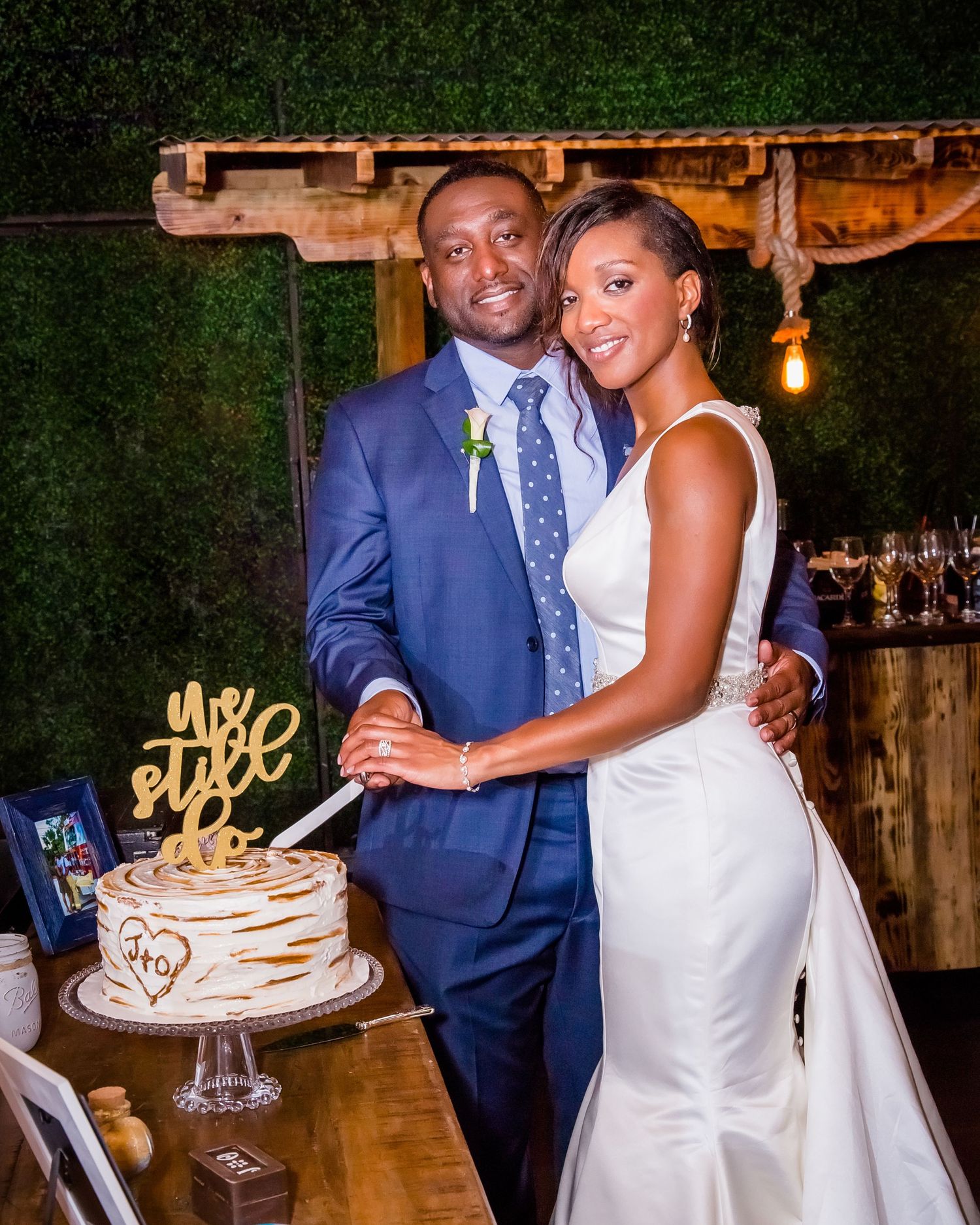 Newlyweds cutting their elegant white wedding cake together at a rustic venue reception.