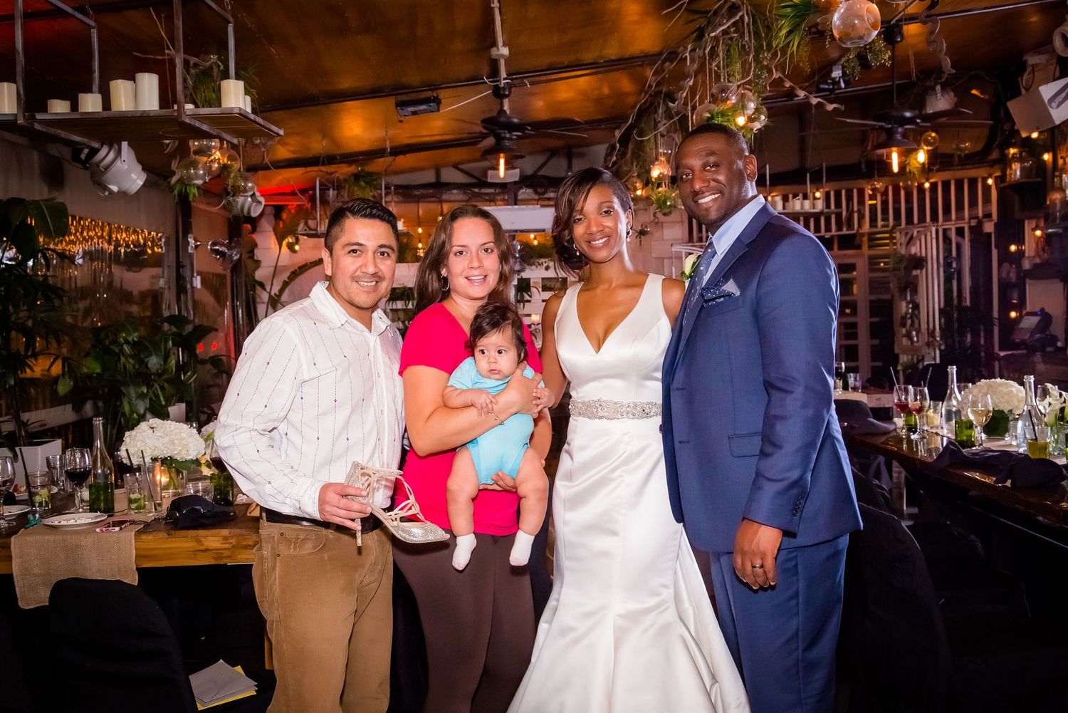 Wedding celebration with guests posing together in a warmly lit indoor venue with decorative lighting.