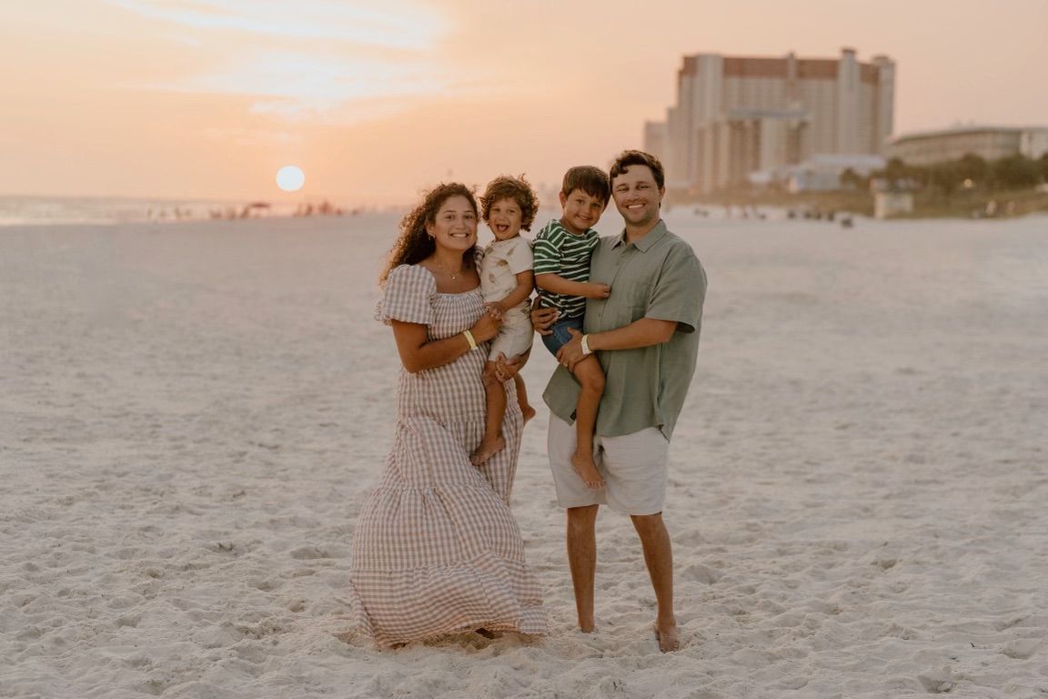 Family portrait on beach at sunset with ocean and building in background.