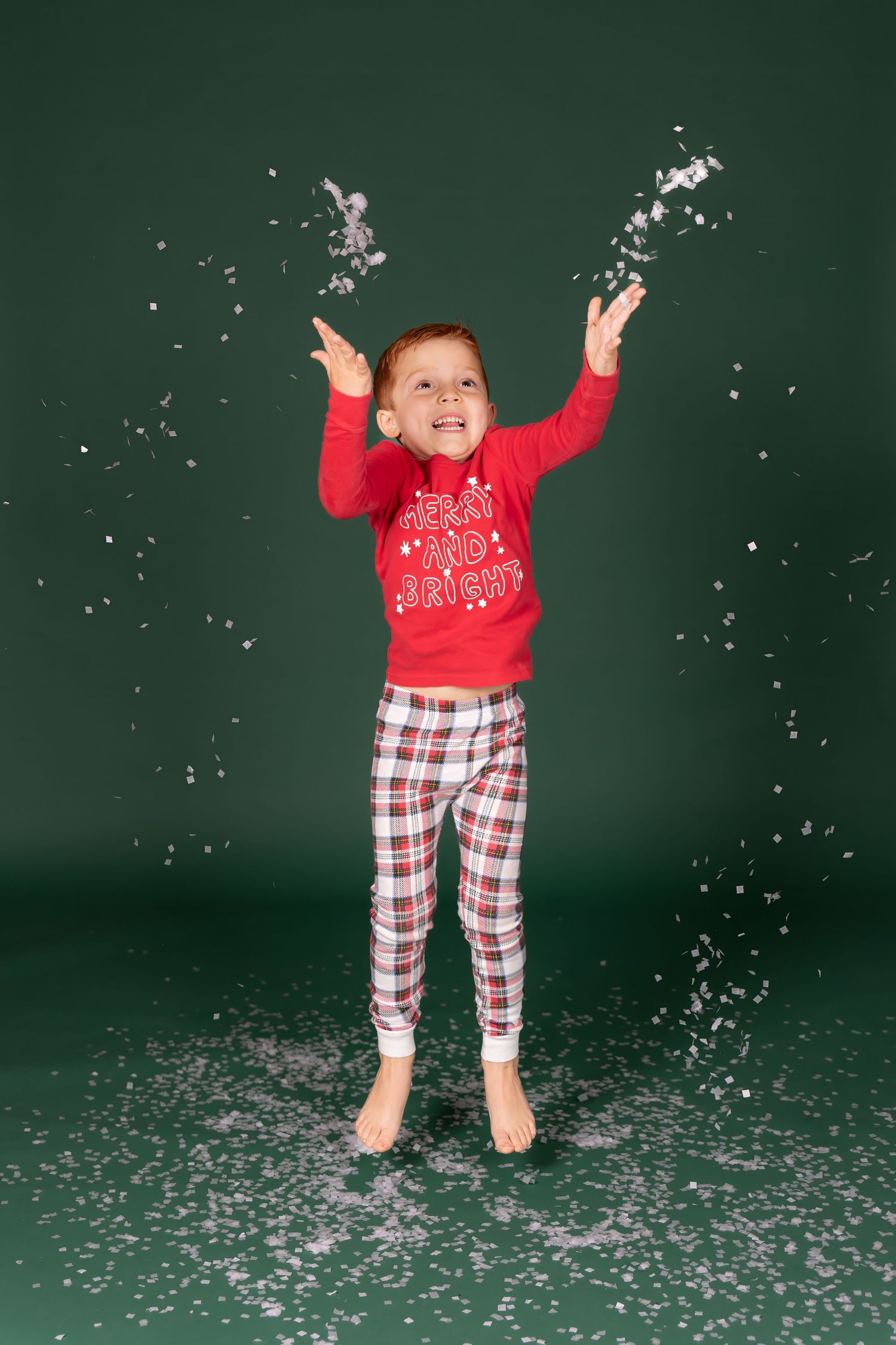 child in christmas pajamas throwing fake snow confetti on a solid green backdrop in studio clayton new jersey Gloucester