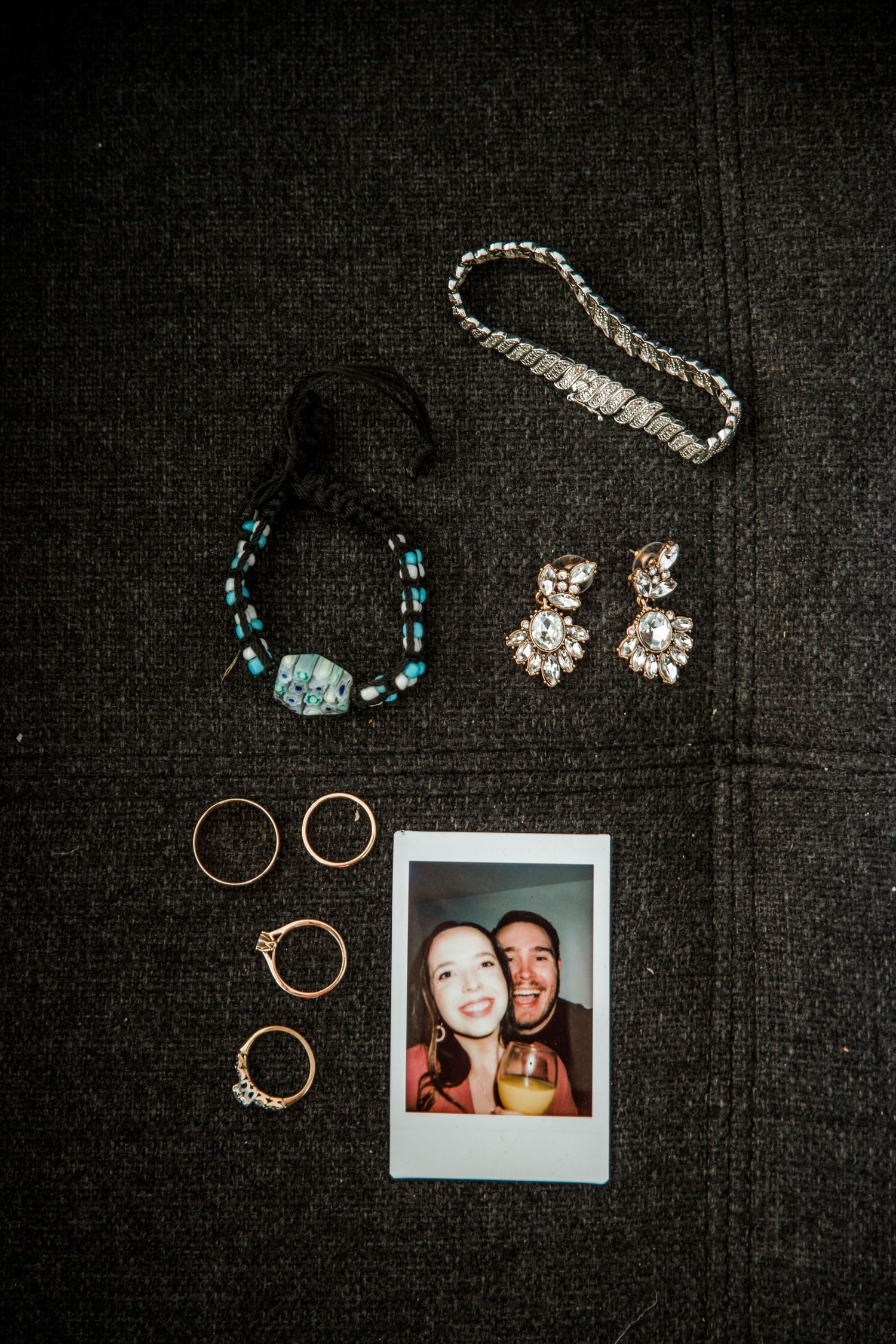 Wedding accessories and jewelry arranged on dark fabric with a polaroid photo.