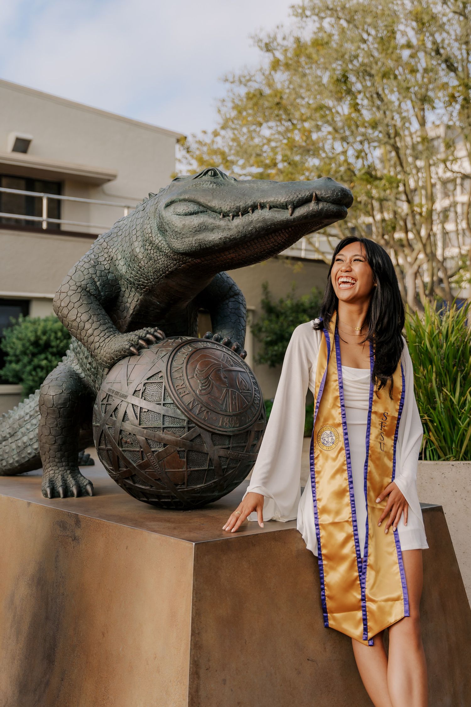 Graduate poses next to alligator statue holding globe on campus grounds.