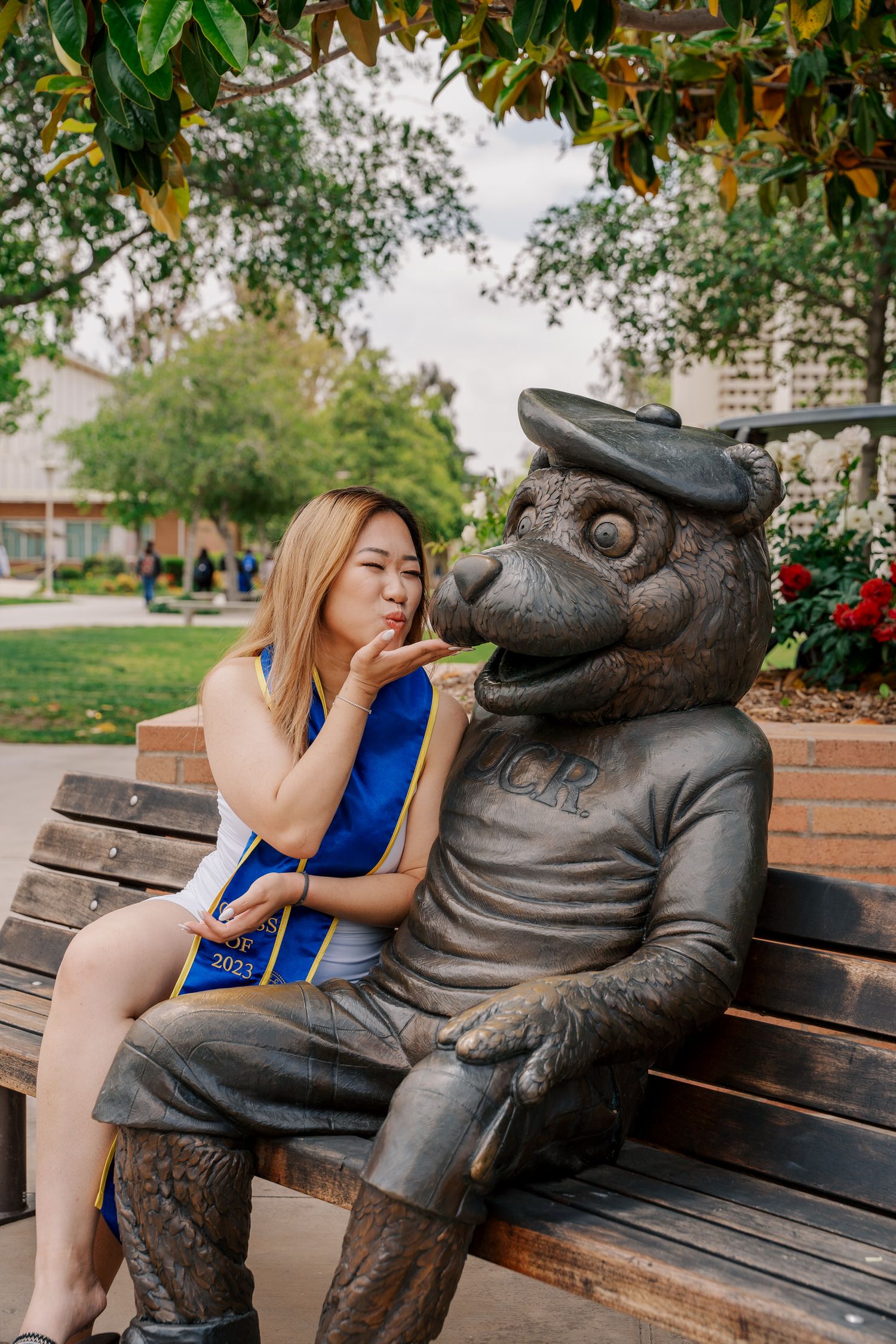 Graduate poses playfully with university mascot statue on campus bench.