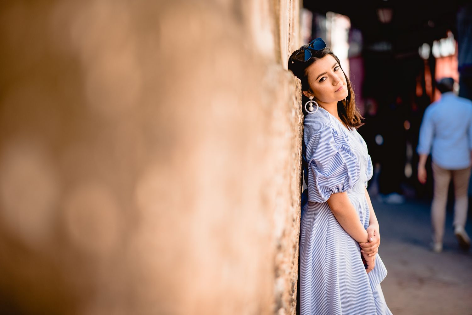 Person in light dress standing beside stone wall in soft lighting.