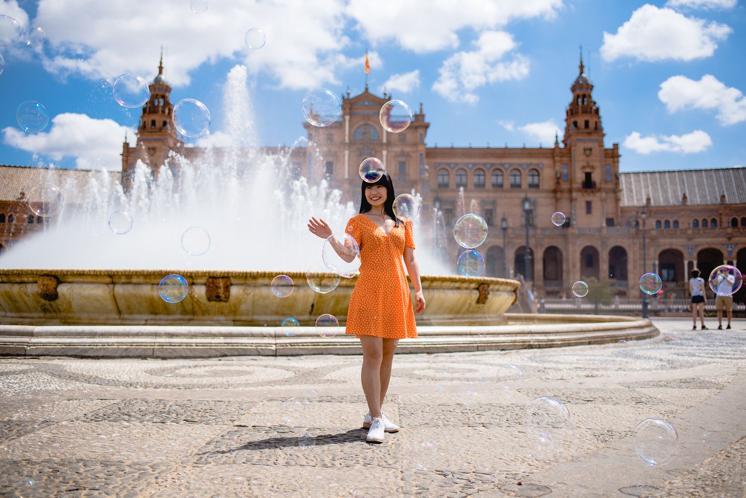 Orange dress contrasts with fountain and historic Spanish plaza architecture.