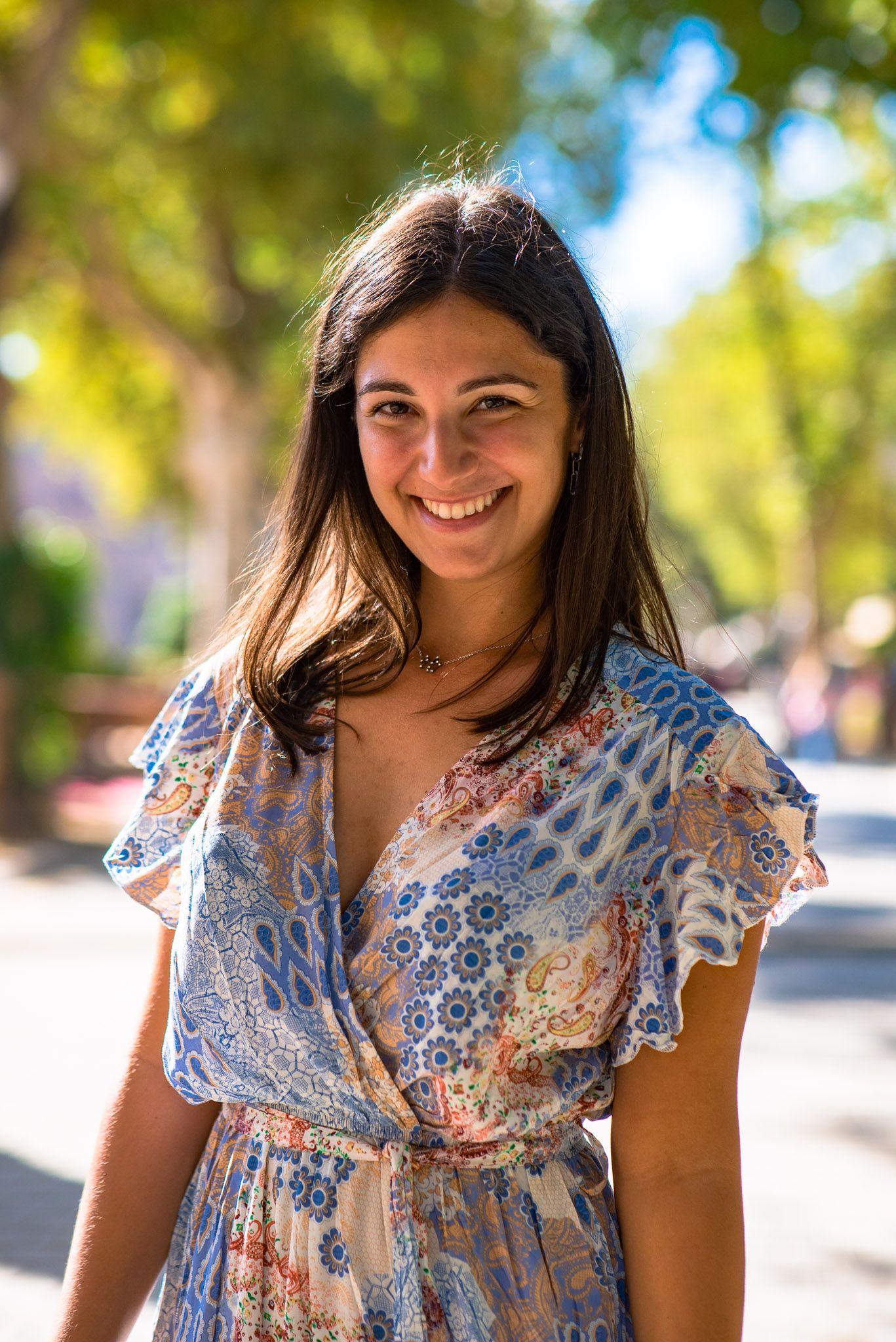 A person wearing a floral print summer dress stands outdoors with soft bokeh lighting in the background.