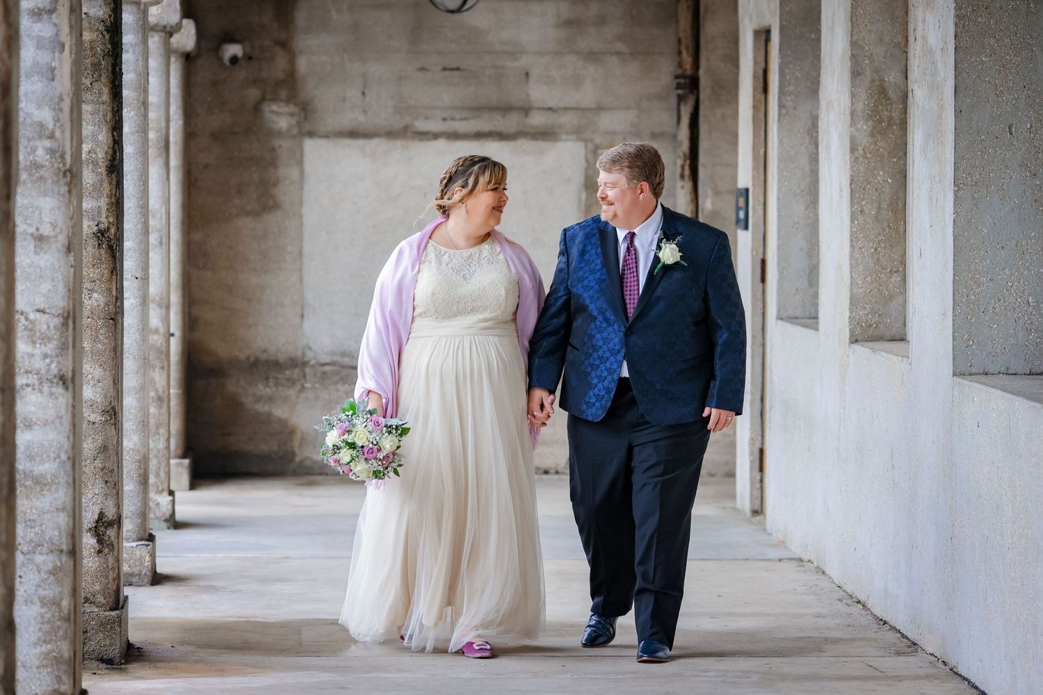 A couple walks together through an elegant columned corridor during their wedding day celebration.