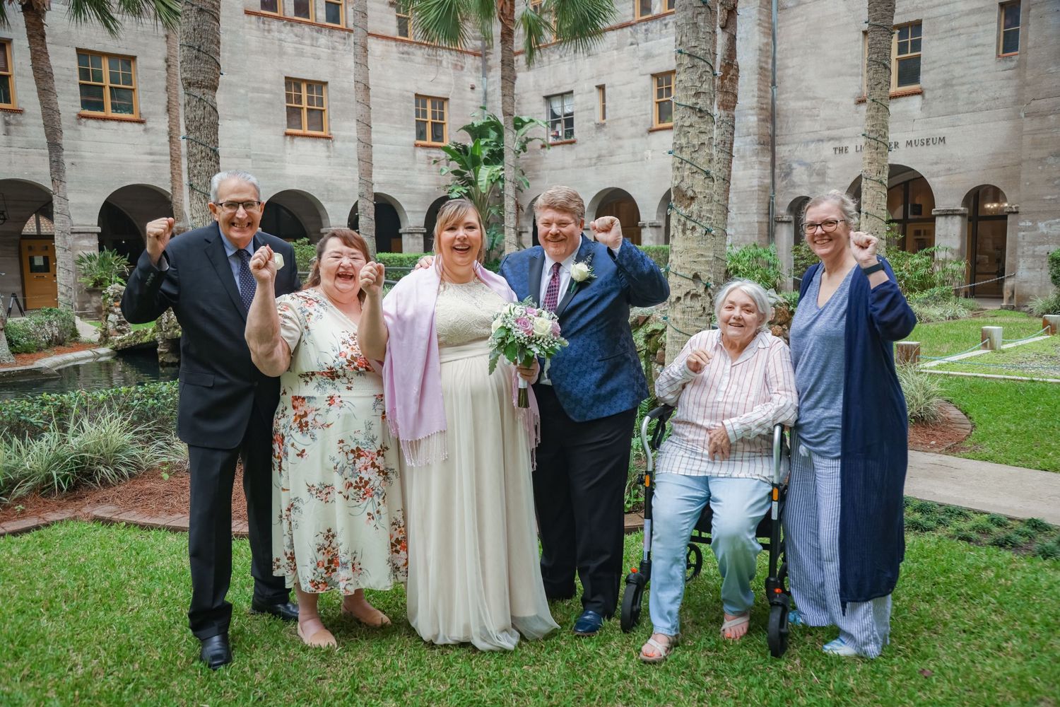 Group photo of wedding party in garden courtyard at historic stone building.
