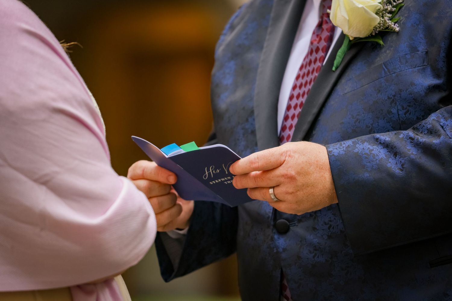Close up of hands exchanging wedding documents with a boutonniere visible.