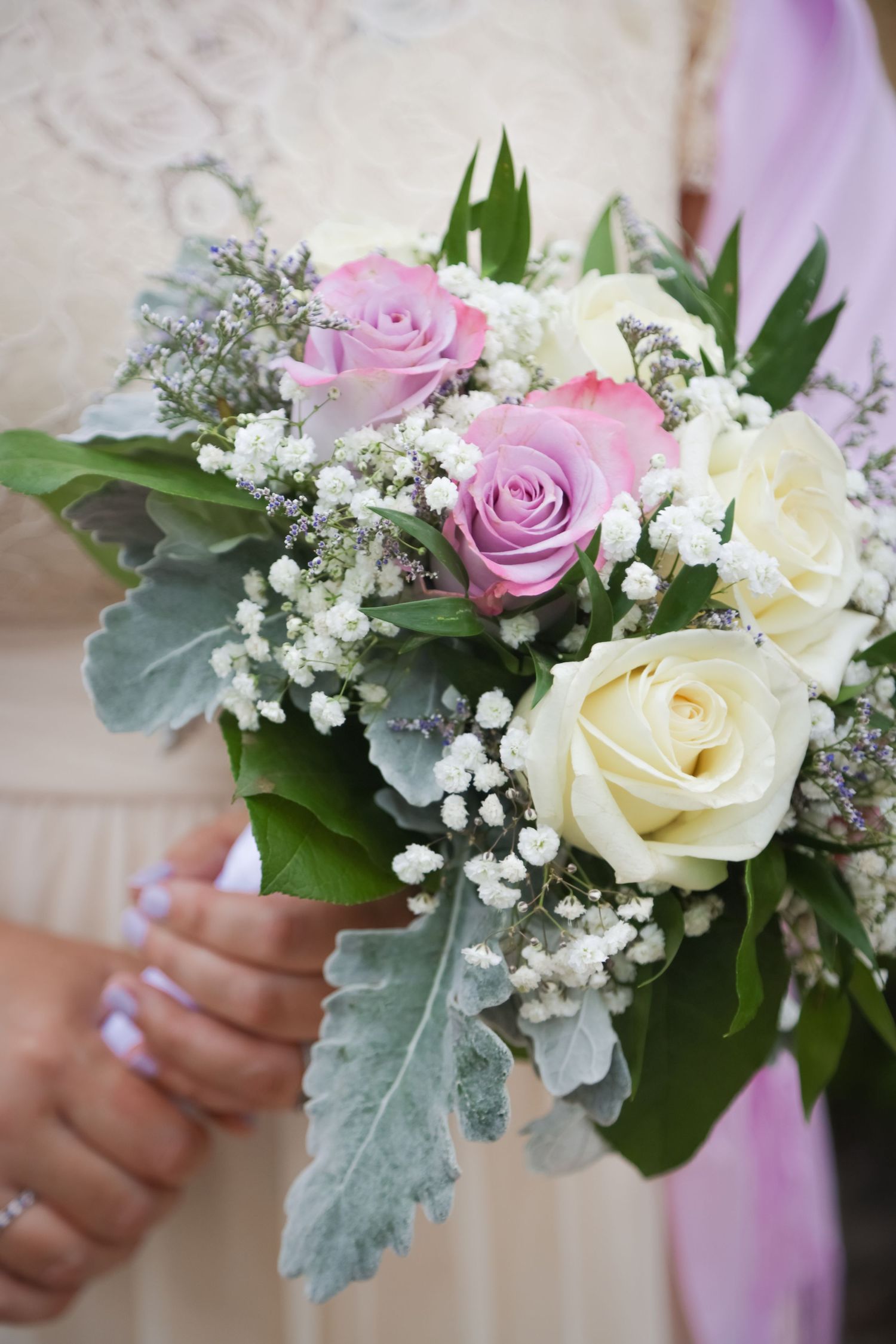 A romantic wedding bouquet featuring pink and white roses with delicate baby's breath and silvery foliage.