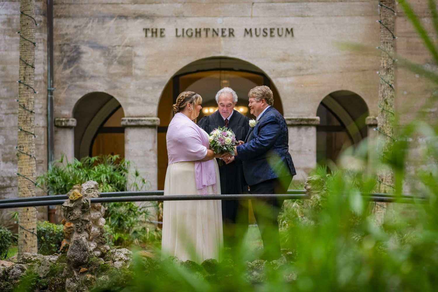 Wedding couple exchanging vows at The Lightner Museum's historic arched entrance.