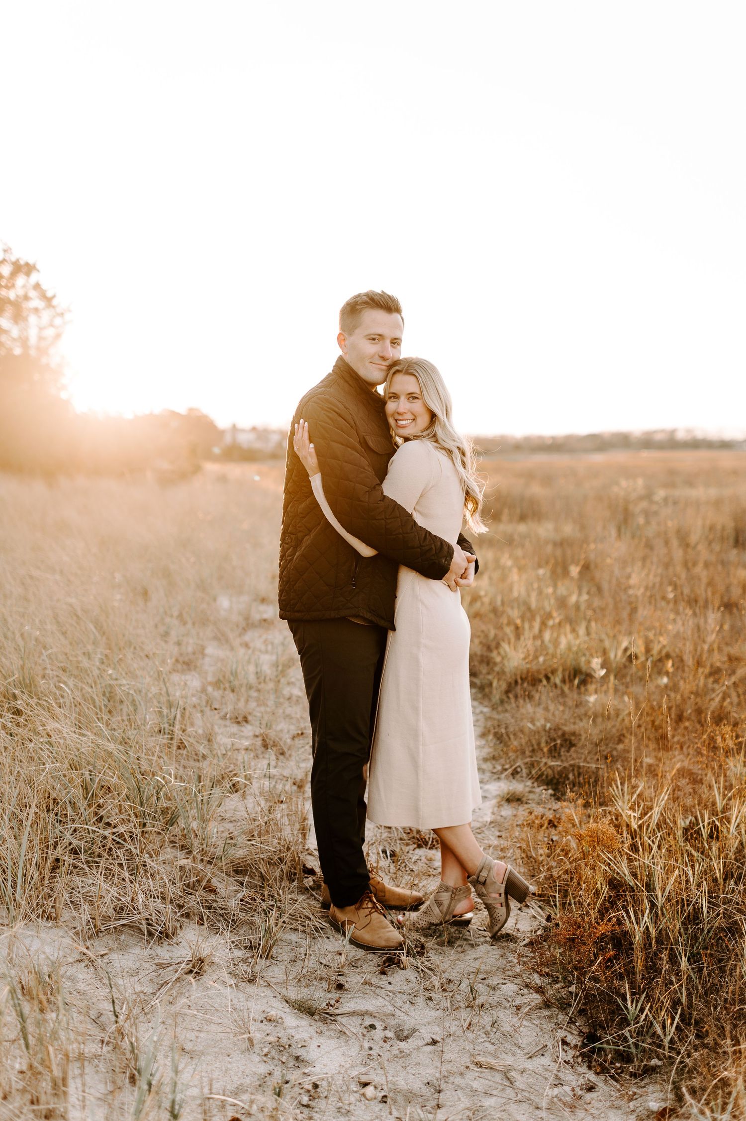 Two people share an intimate moment while standing in tall grass during golden hour.