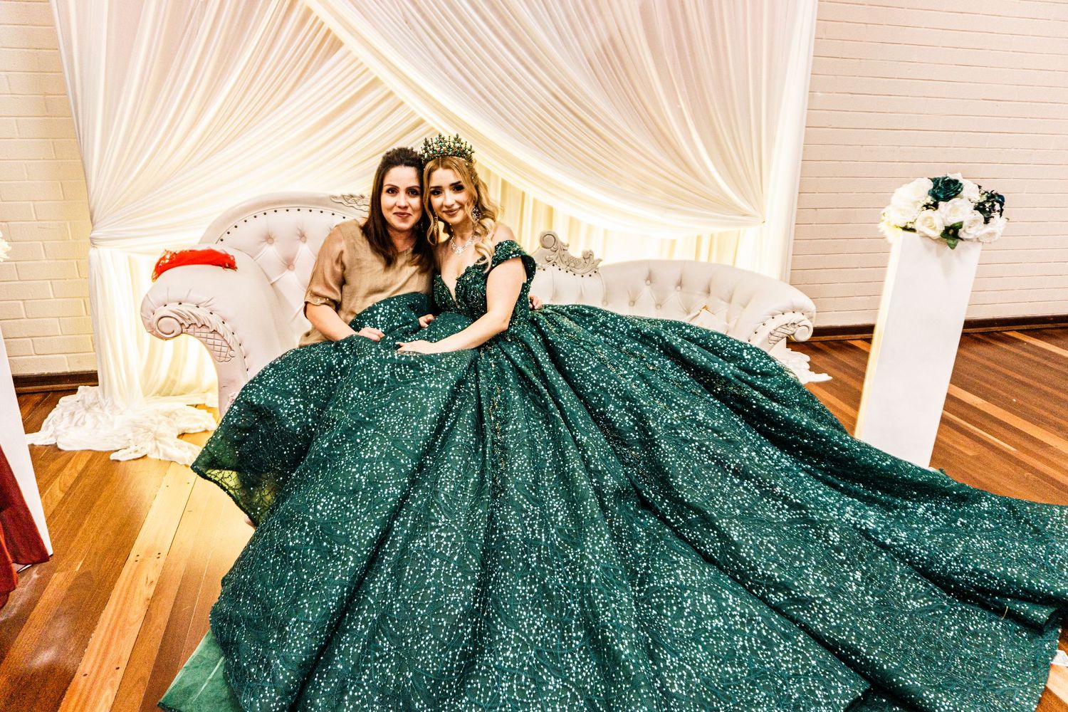 Formal portrait featuring sparkly emerald green ball gown in elegant white draped setting.