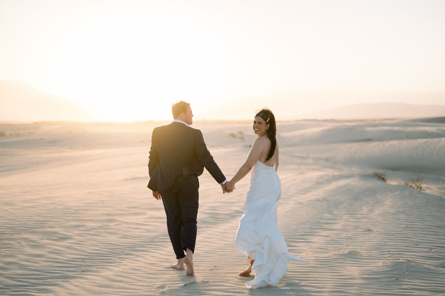A couple walking hand in hand on sand dunes at sunset.