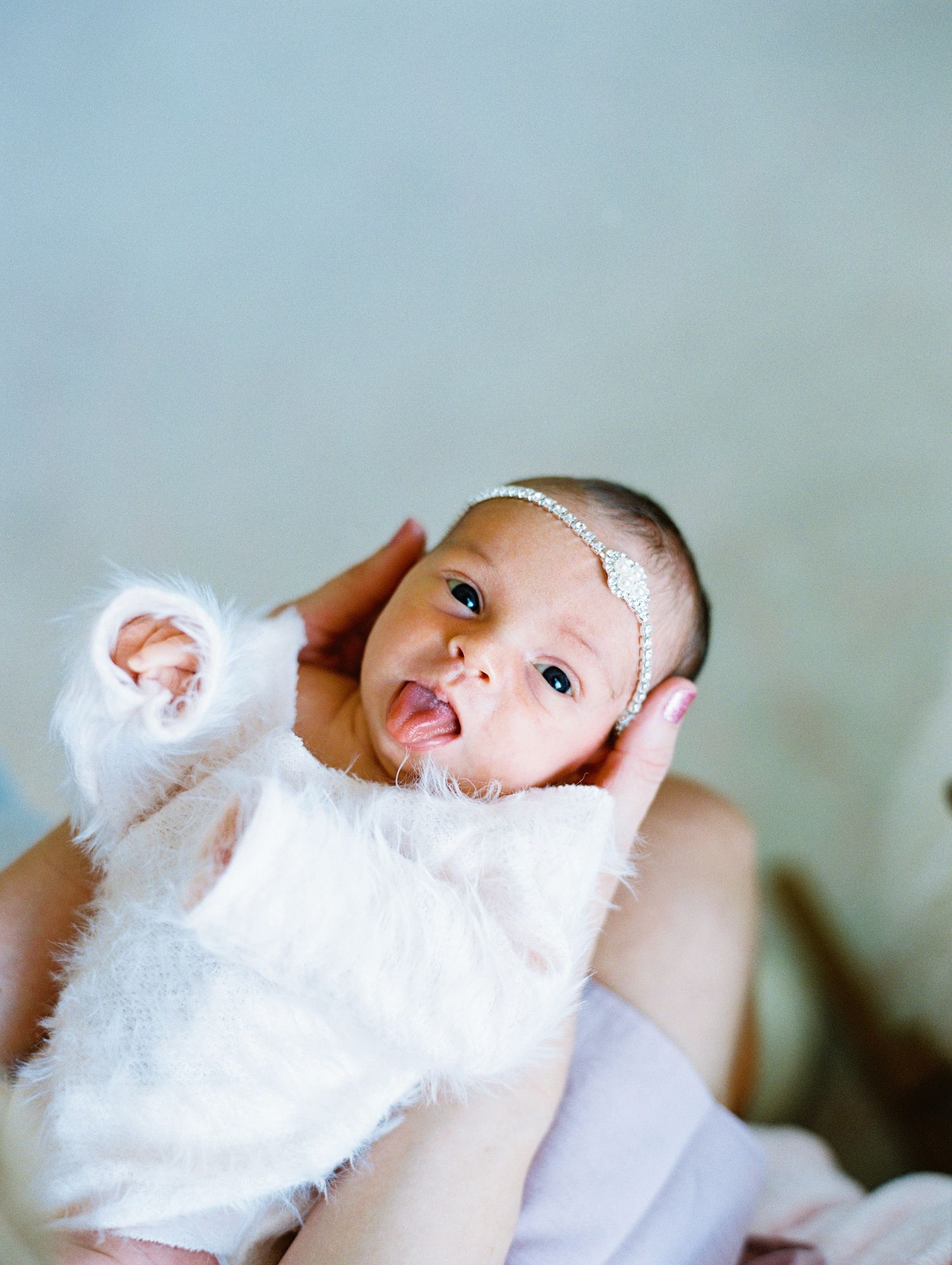 Baby wearing white outfit and pearl headband making an expressive face.