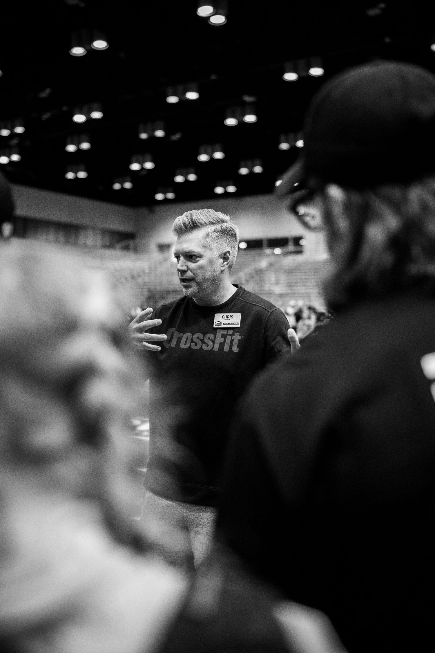 Coach giving instructions during CrossFit competition in indoor arena.