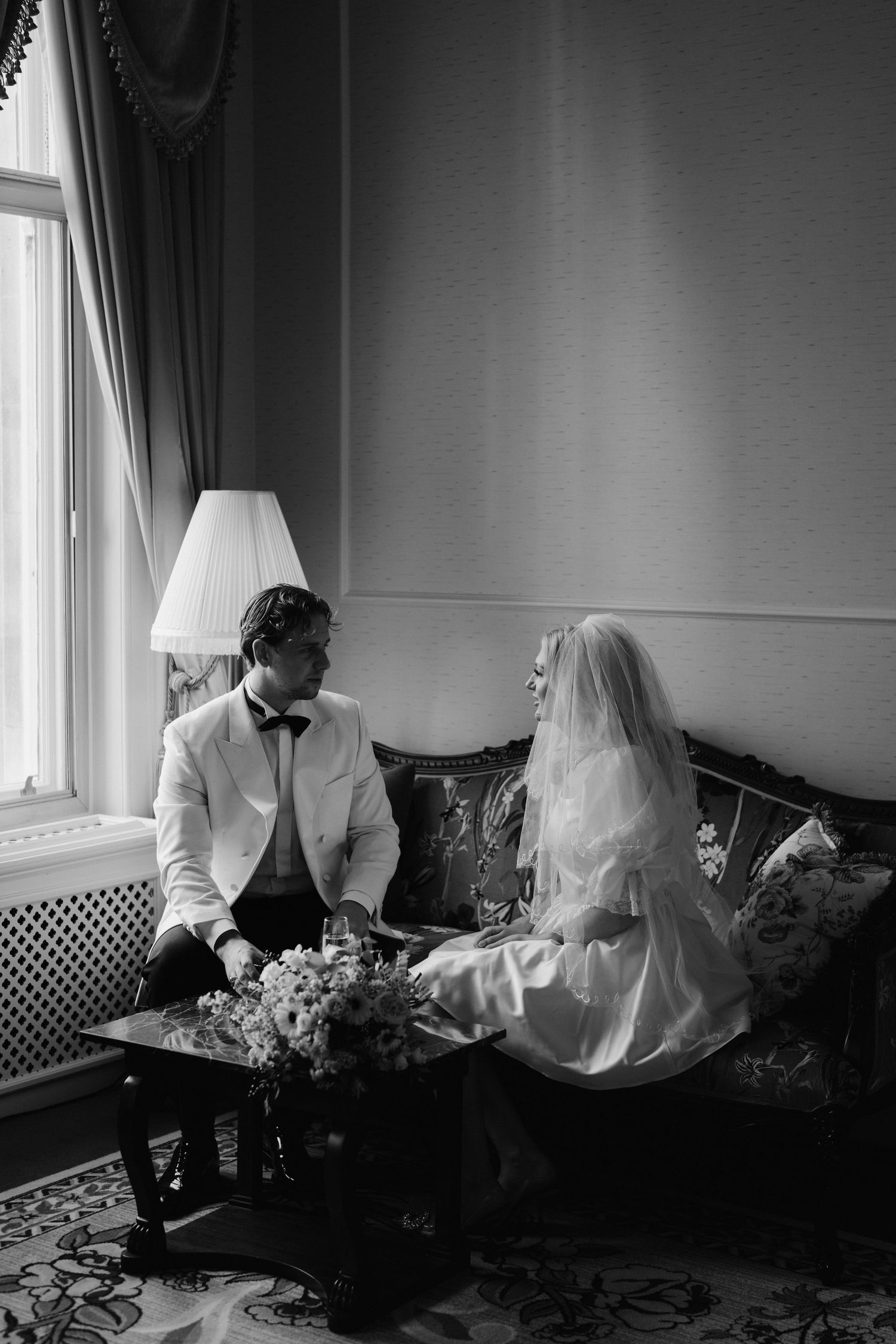 bride and groom sat on sofa drinking champagne at the Randolph hotel in oxford
