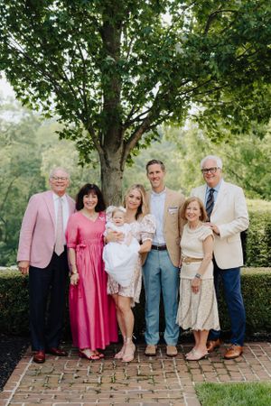Multi-generational family gathering outdoors for a formal portrait under a leafy green tree.