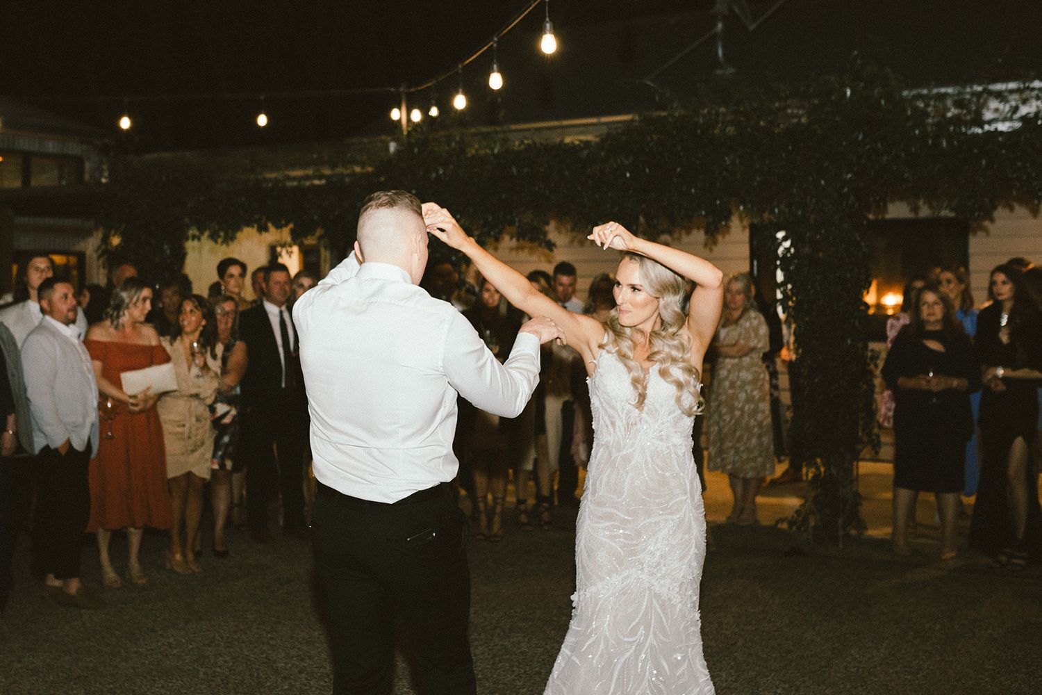 Couple dancing at their outdoor evening wedding reception under string lights.