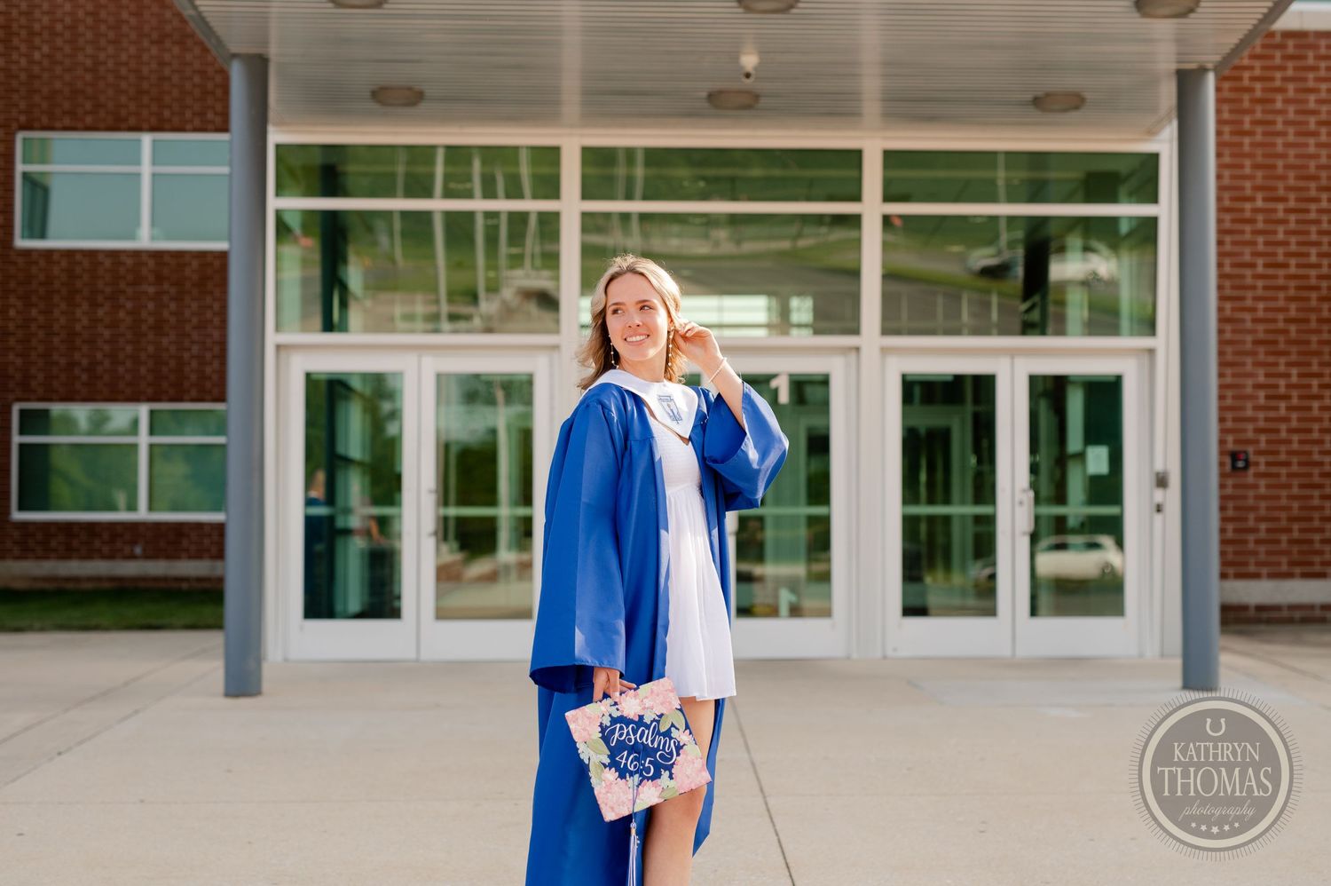 Graduate in blue cap and gown poses in front of Spring Grove Area High School entrance.