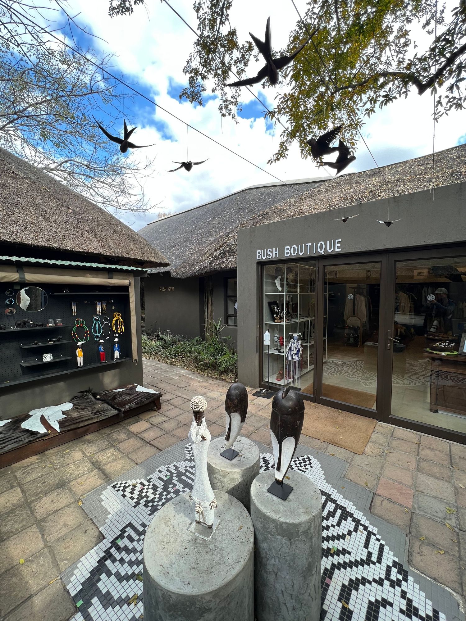 Boutique shop entrance with thatched roof and decorative bird silhouettes hanging above stone courtyard.