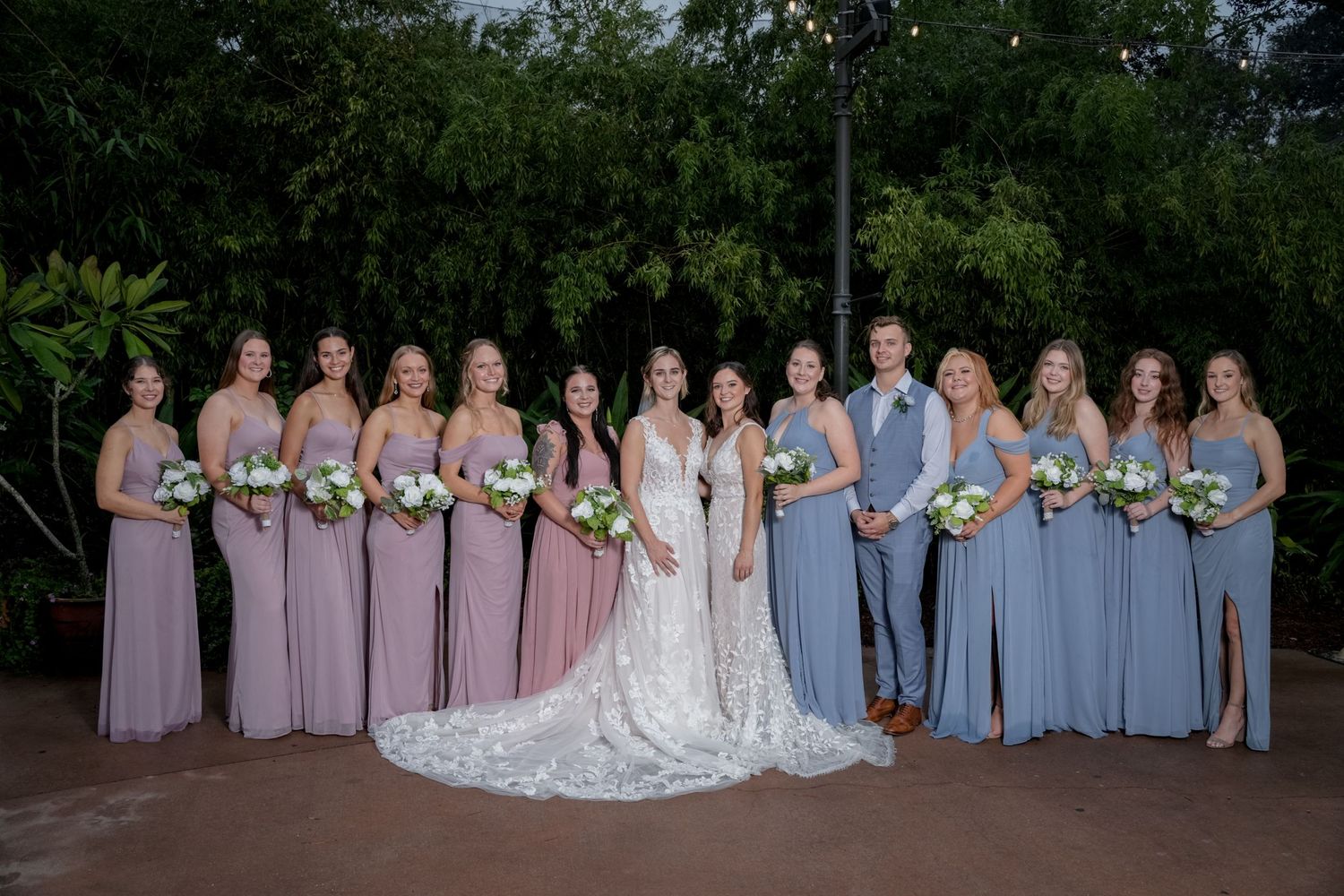 Wedding party poses outdoors with bridesmaids in purple and blue dresses.
