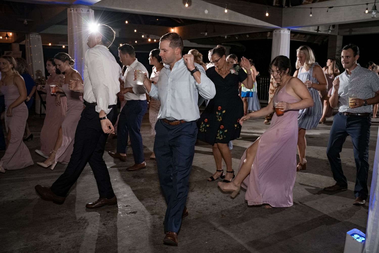 Wedding reception dance party with guests dancing in a dimly lit venue.