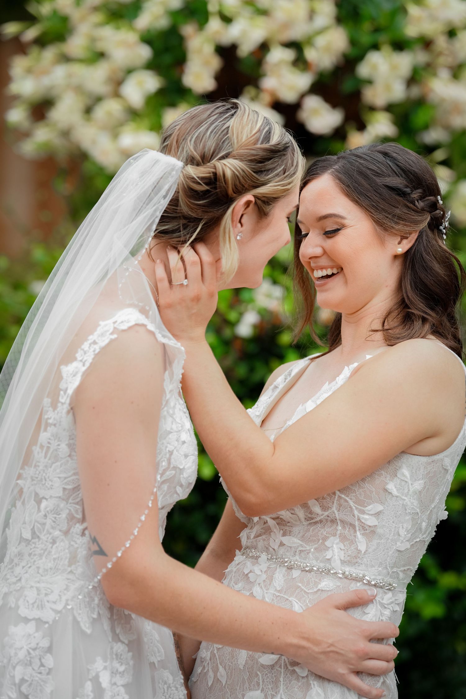 Two brides in matching white lace dresses share an intimate moment outdoors.