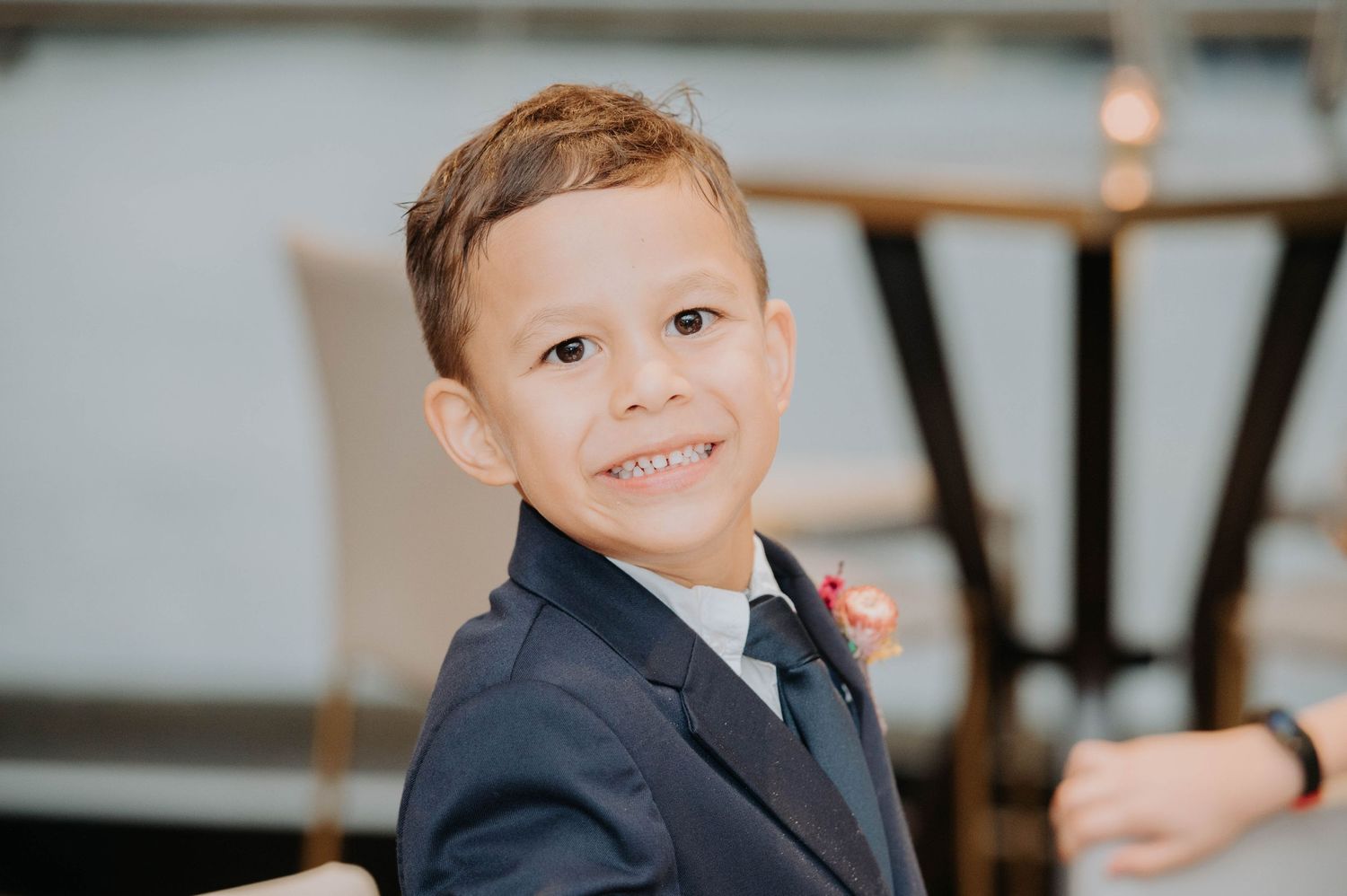 Young ring bearer in a navy suit and tie smiles at a wedding celebration.