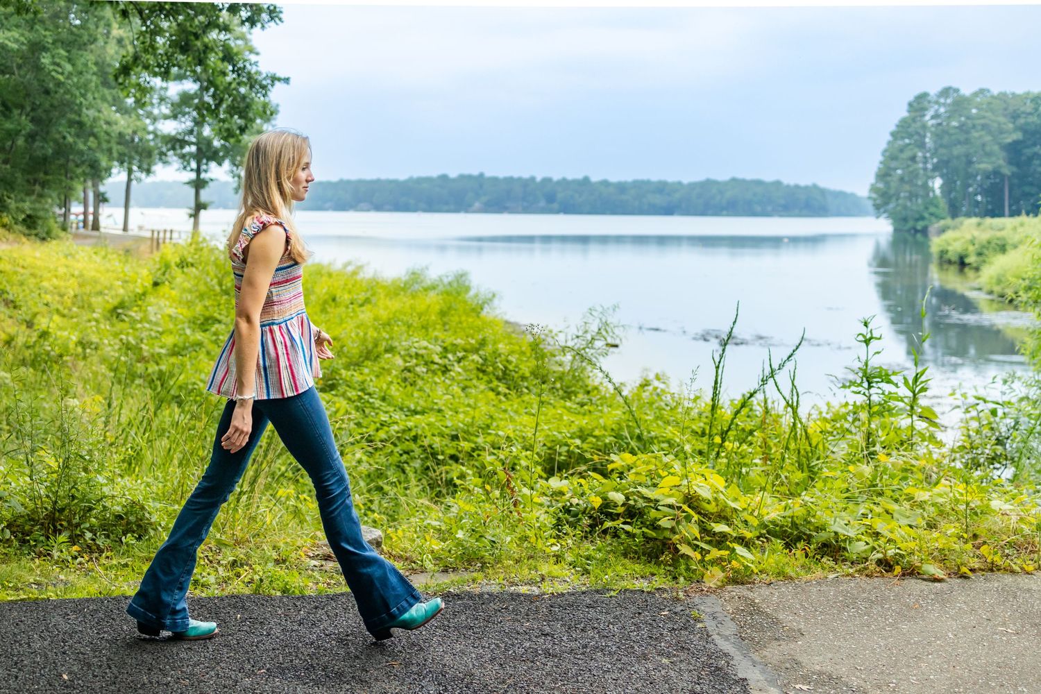 Walking along lakeside path in striped top and jeans on sunny summer day.