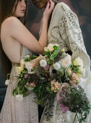 A large opulent floral bouquet with a wedding couple standing in teh bakcground.