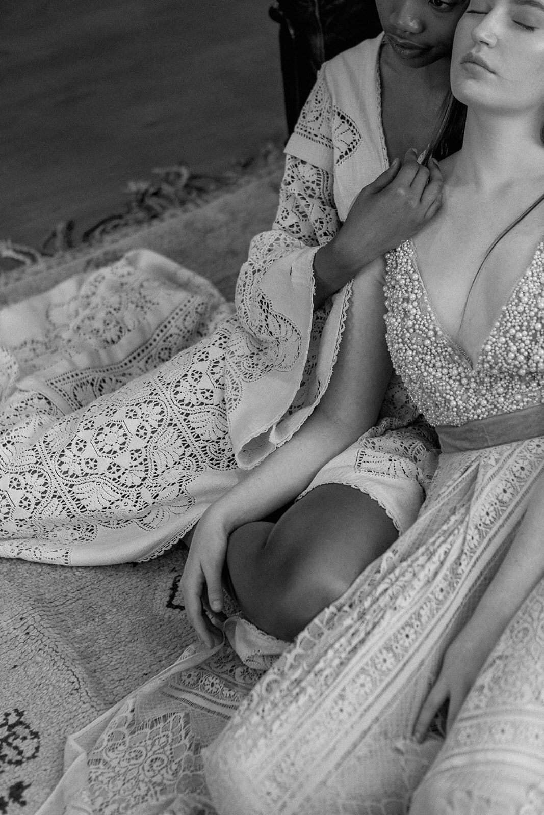 A monochrome portrait of a LGBTQ couple sitting on the floor in their wedding dresses.