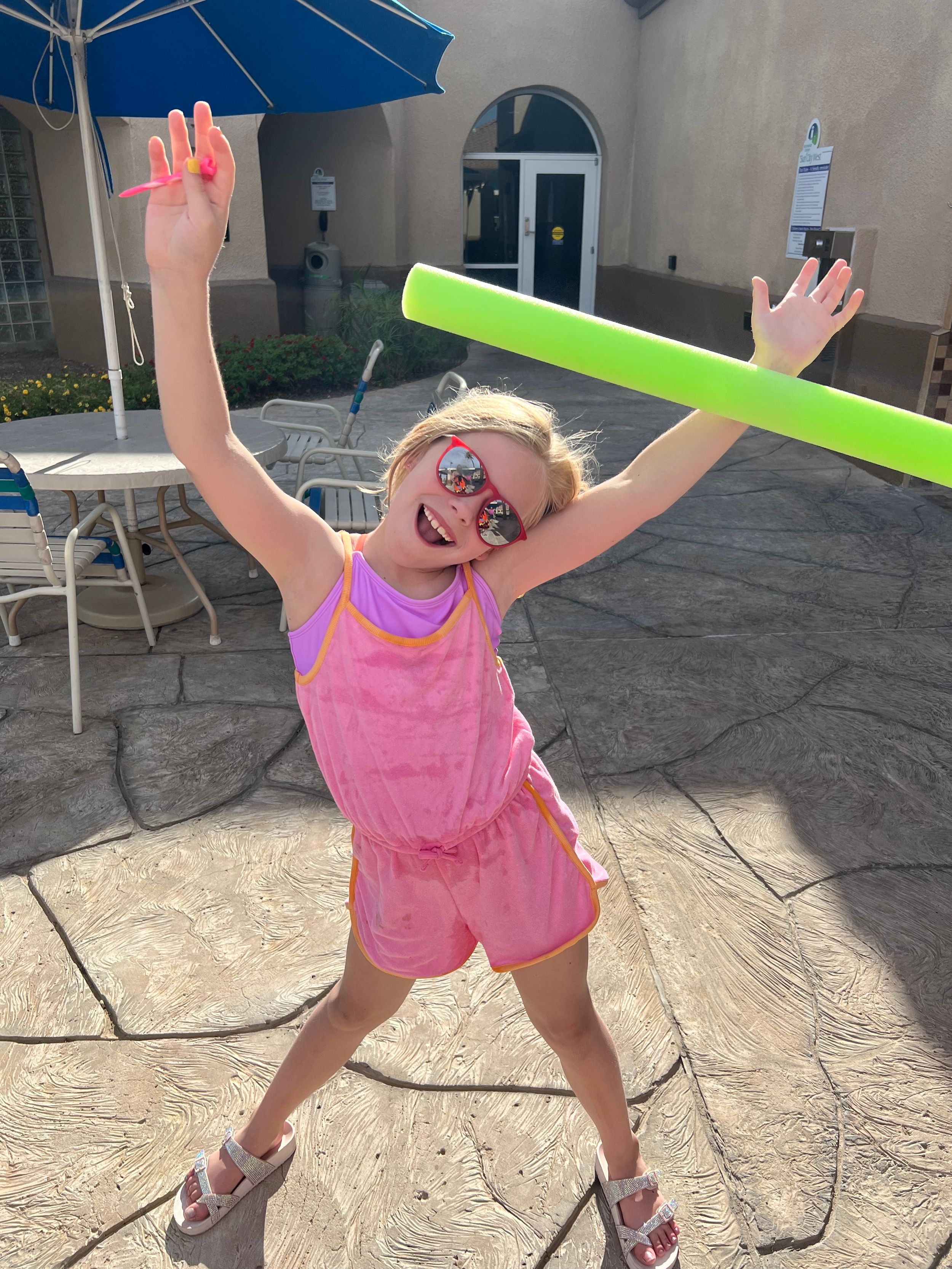 Child in pink outfit jumping joyfully on outdoor patio.