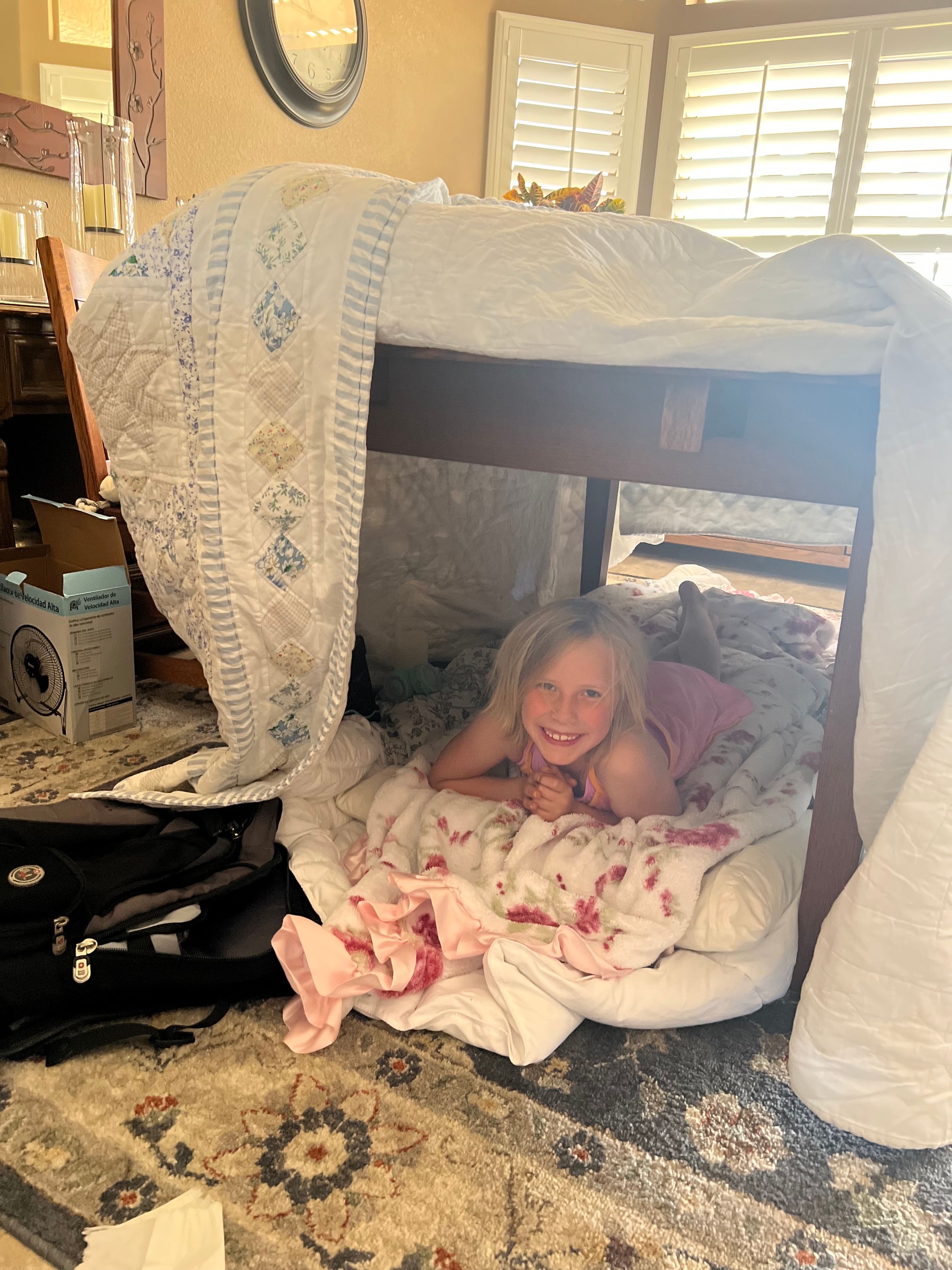 Child playing hide and seek under a blanket fort.