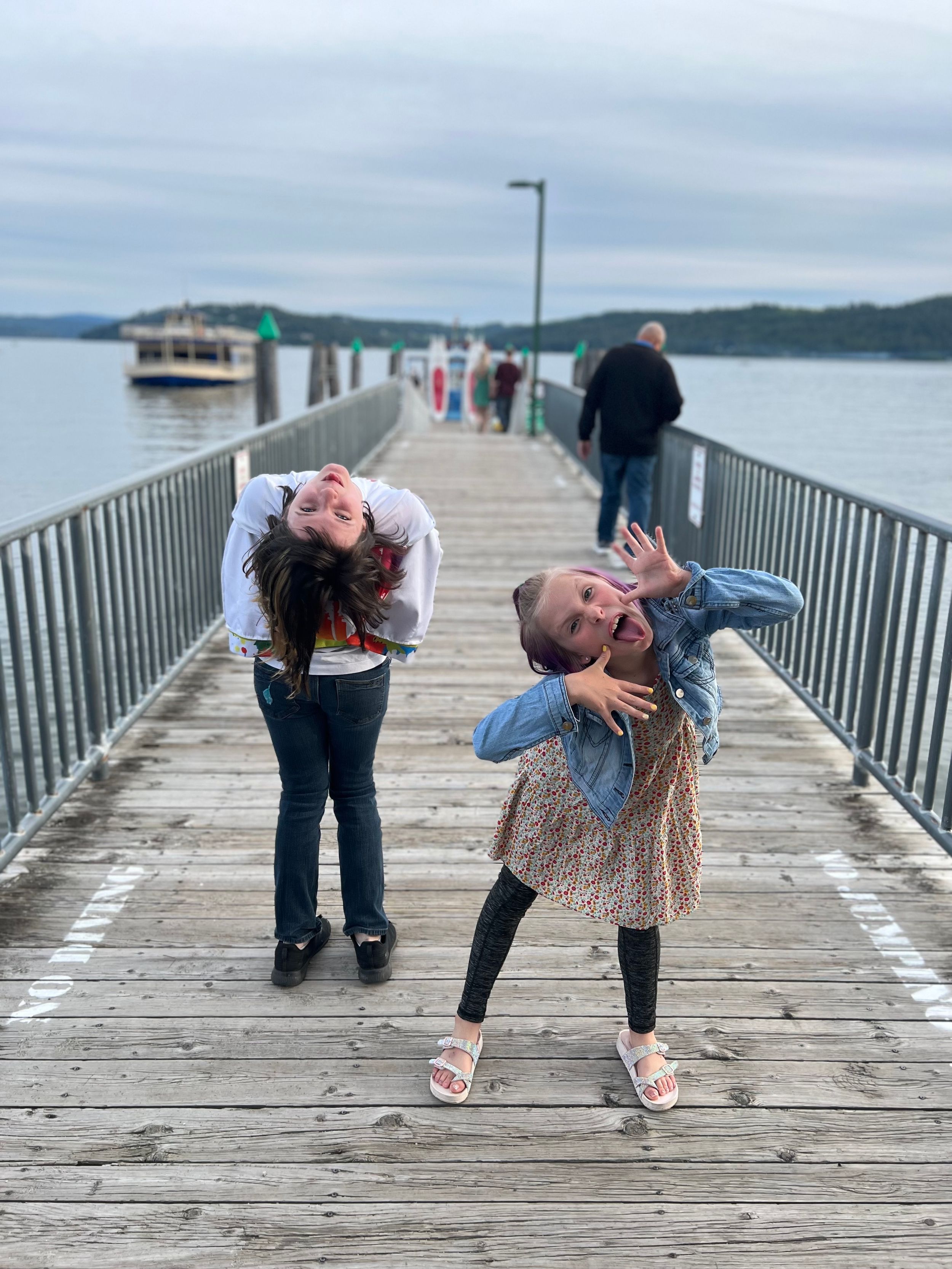 Playful poses on a wooden pier overlooking water and mountains.