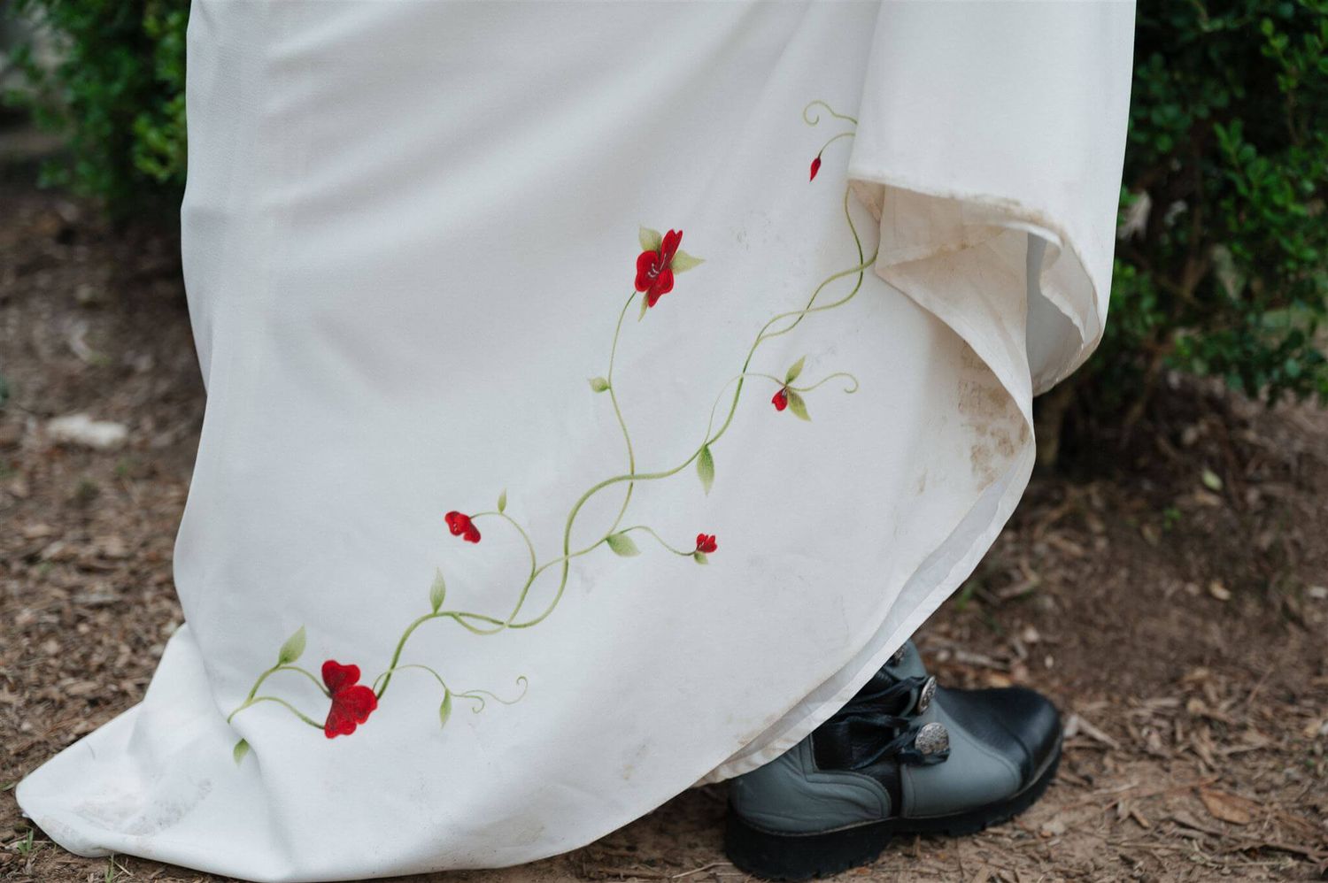 Detail shot of white dress hem with delicate red floral embroidery and black boots.