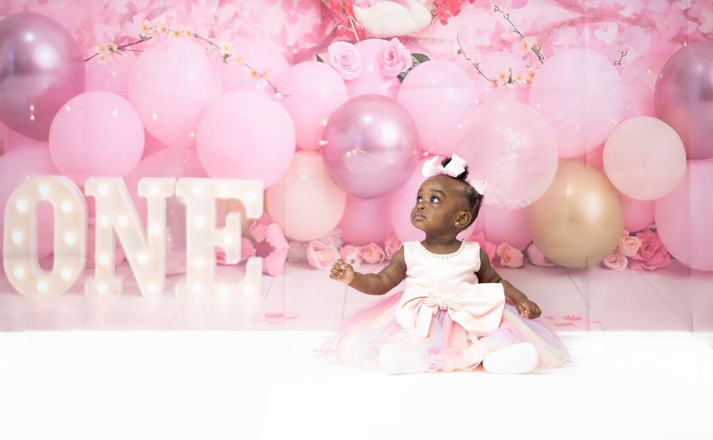 Pink and gold balloon backdrop with glowing ONE sign for first birthday photo shoot.