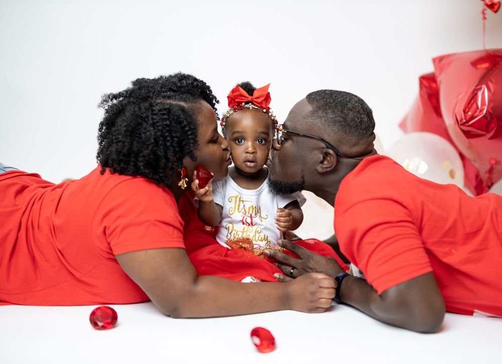Family wearing matching red outfits poses with rose petals on white backdrop for professional photo shoot.