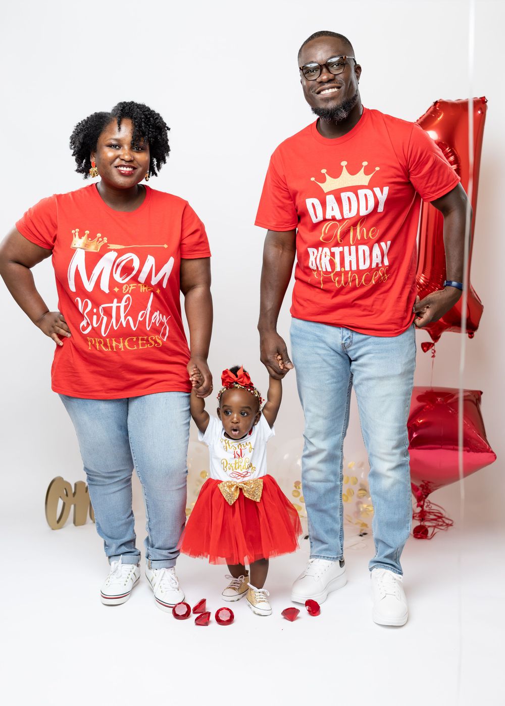 Family in matching red shirts and jeans poses against white backdrop with festive decorations.