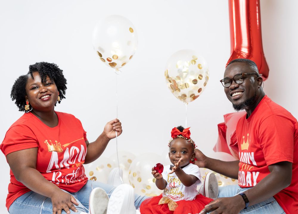 Family celebrates with gold confetti and balloons in coordinated red outfits against white background.
