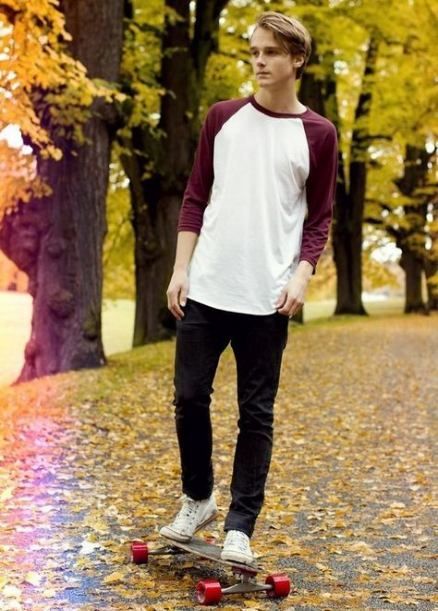 Person skateboarding in autumn scene wearing burgundy baseball shirt and dark jeans.