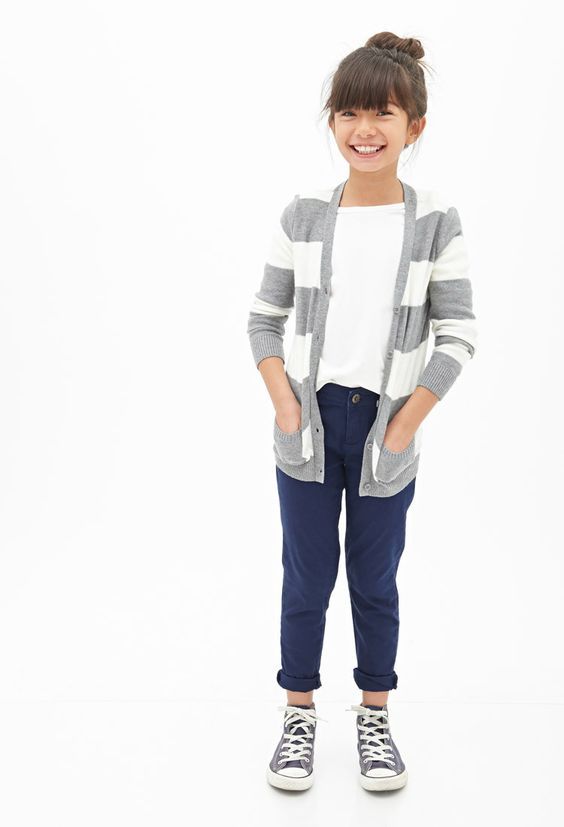 Child in striped gray cardigan and navy pants with classic sneakers against white background.